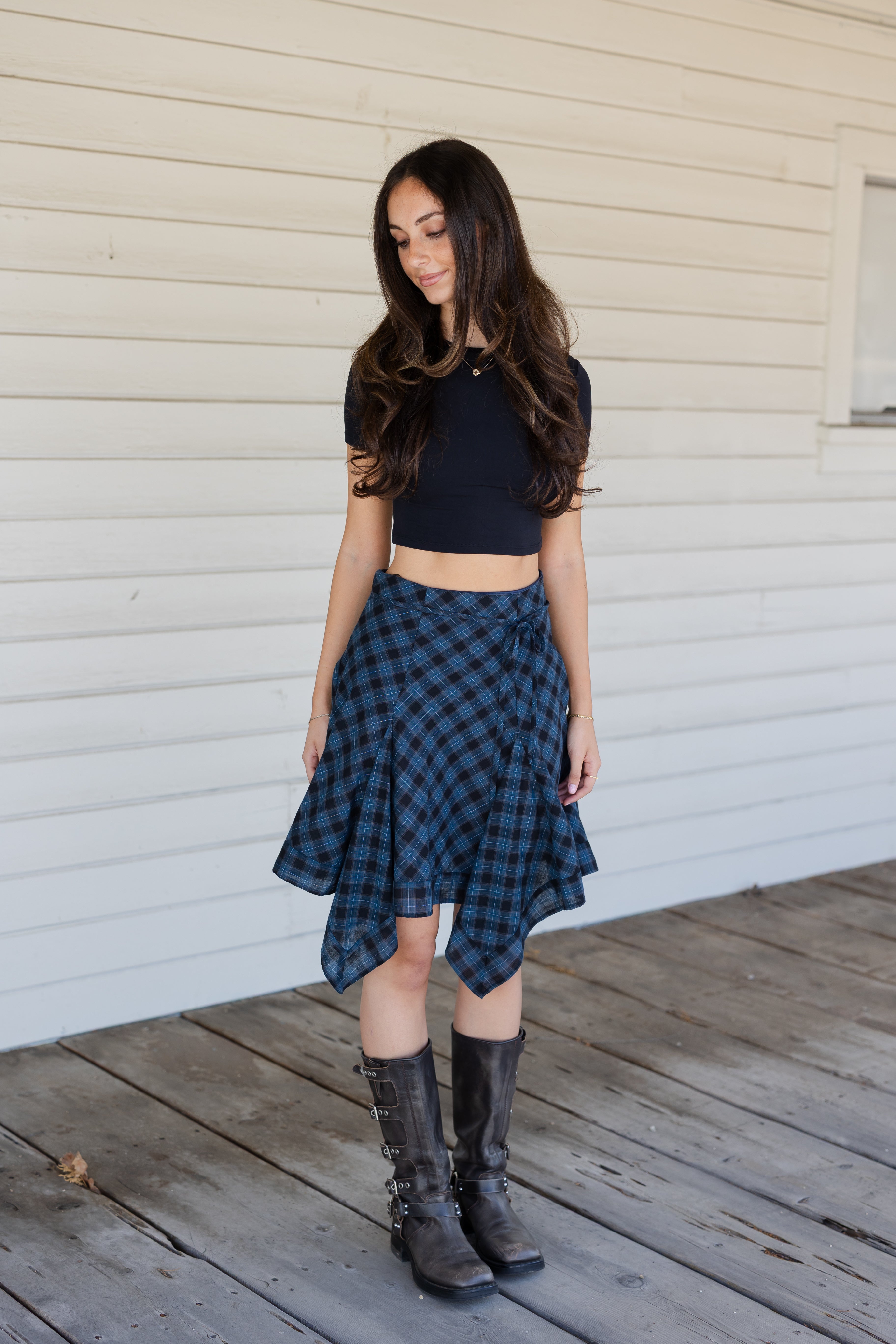 Woman wearing a black top and plaid skirt standing on a wooden deck.