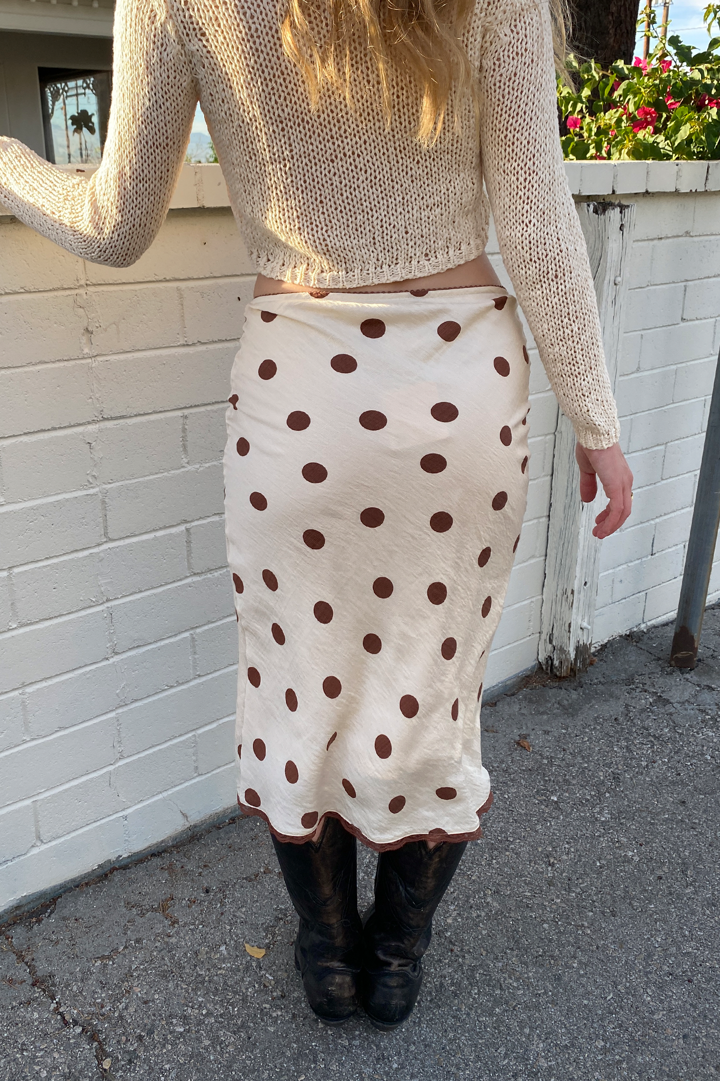 Person wearing a beige sweater and polka dot skirt against a white wall.