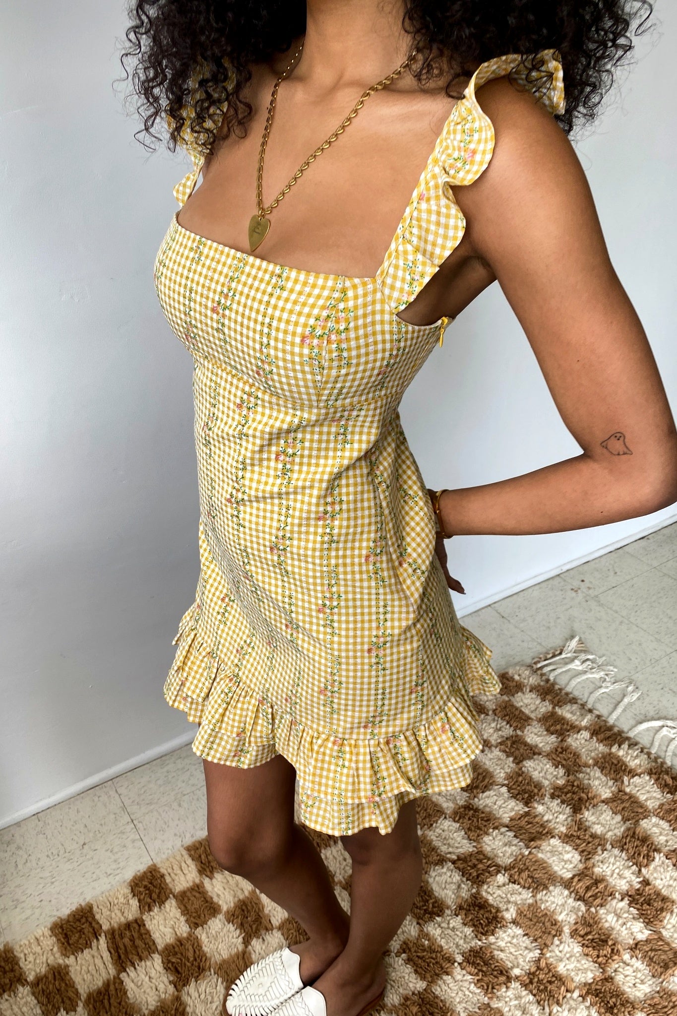Woman wearing a yellow checkered dress standing on a checkered rug.