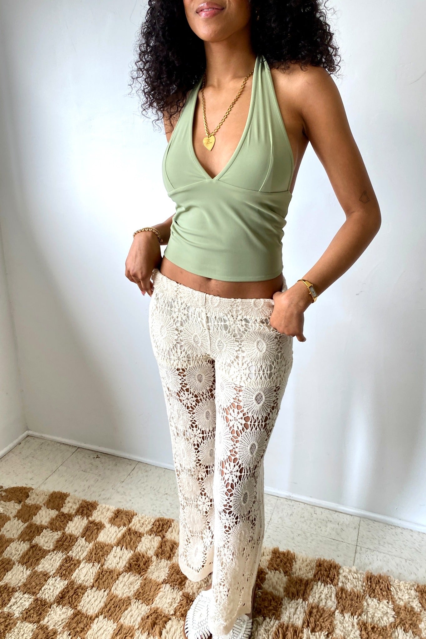 Woman wearing a green top and white lace pants standing on a checkered floor.