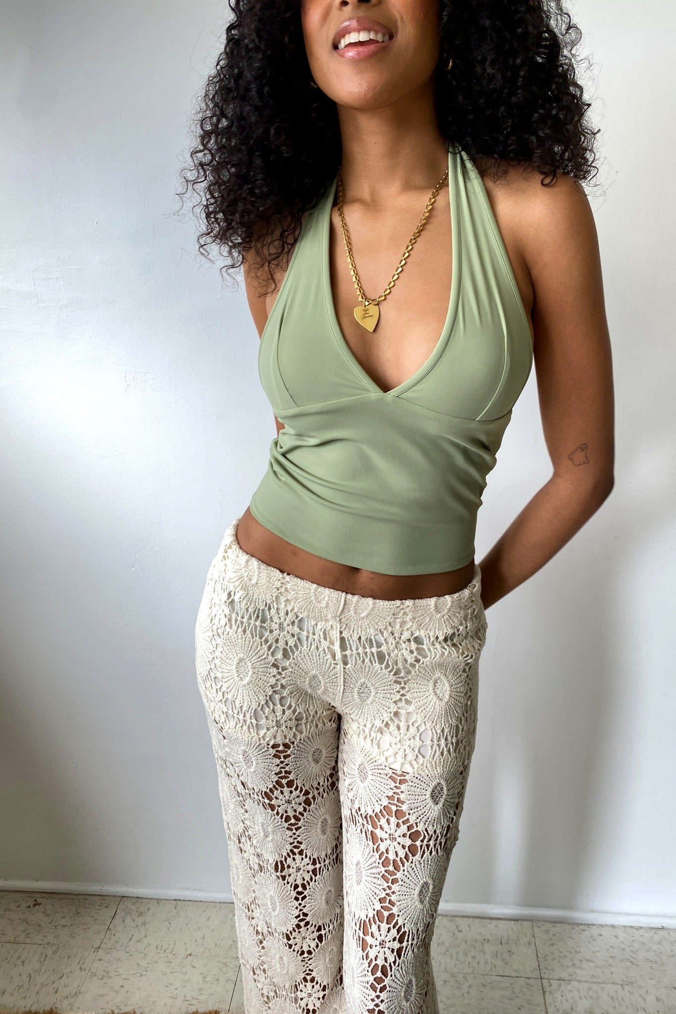 Woman wearing a green top and white lace pants against a plain background