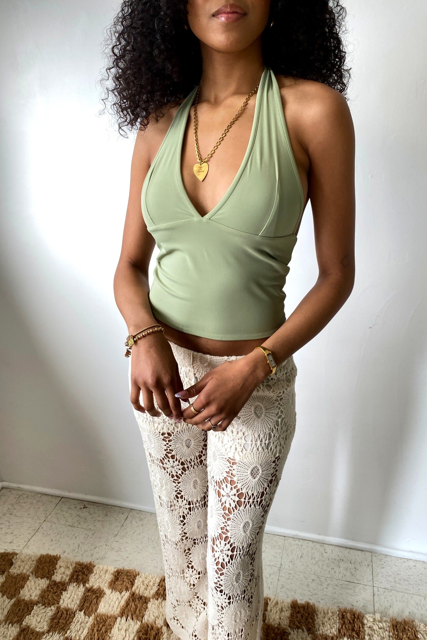 Woman wearing a green halter top and white lace pants against a plain background