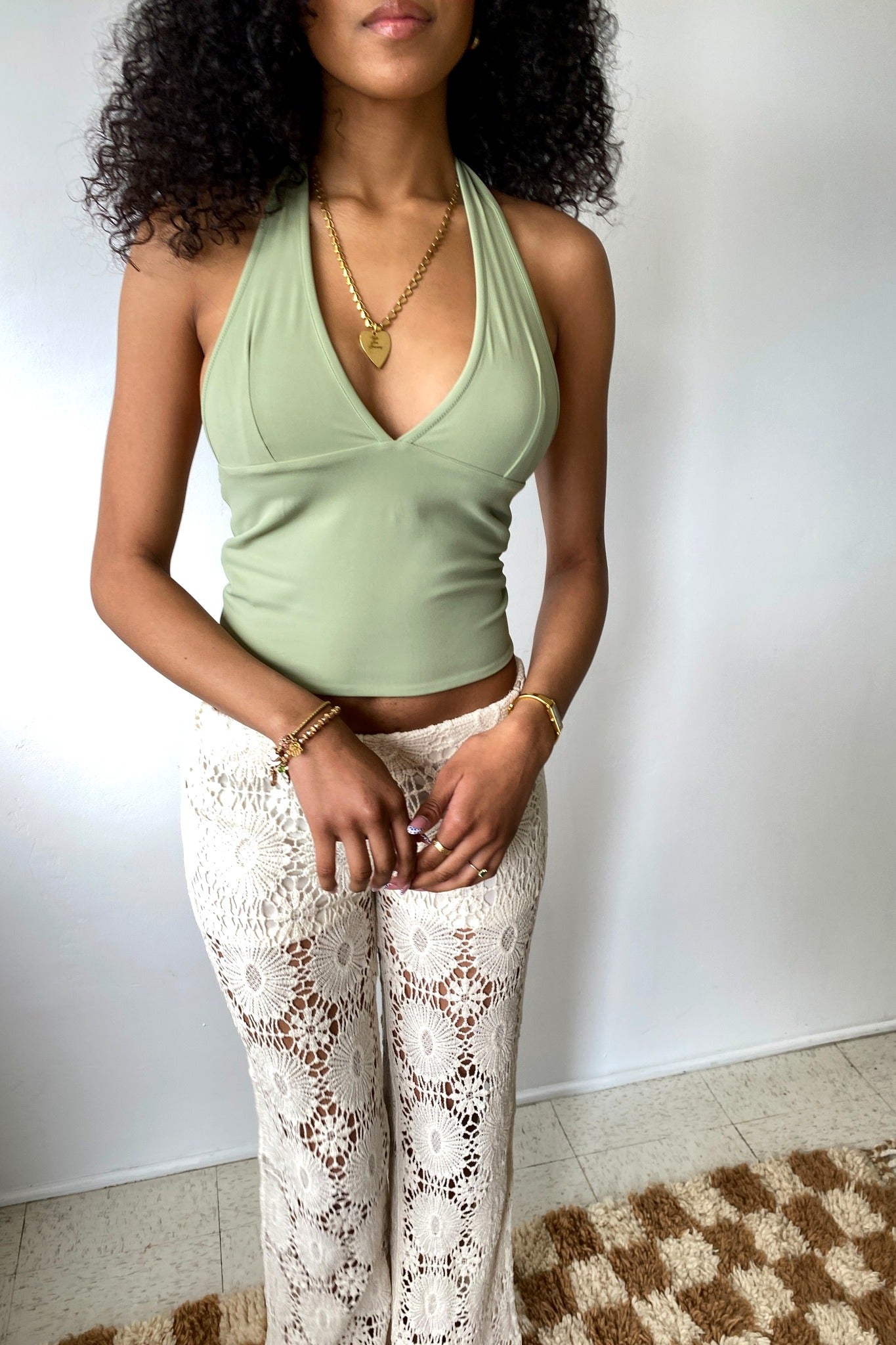Woman wearing a green halter top and white lace pants against a plain background