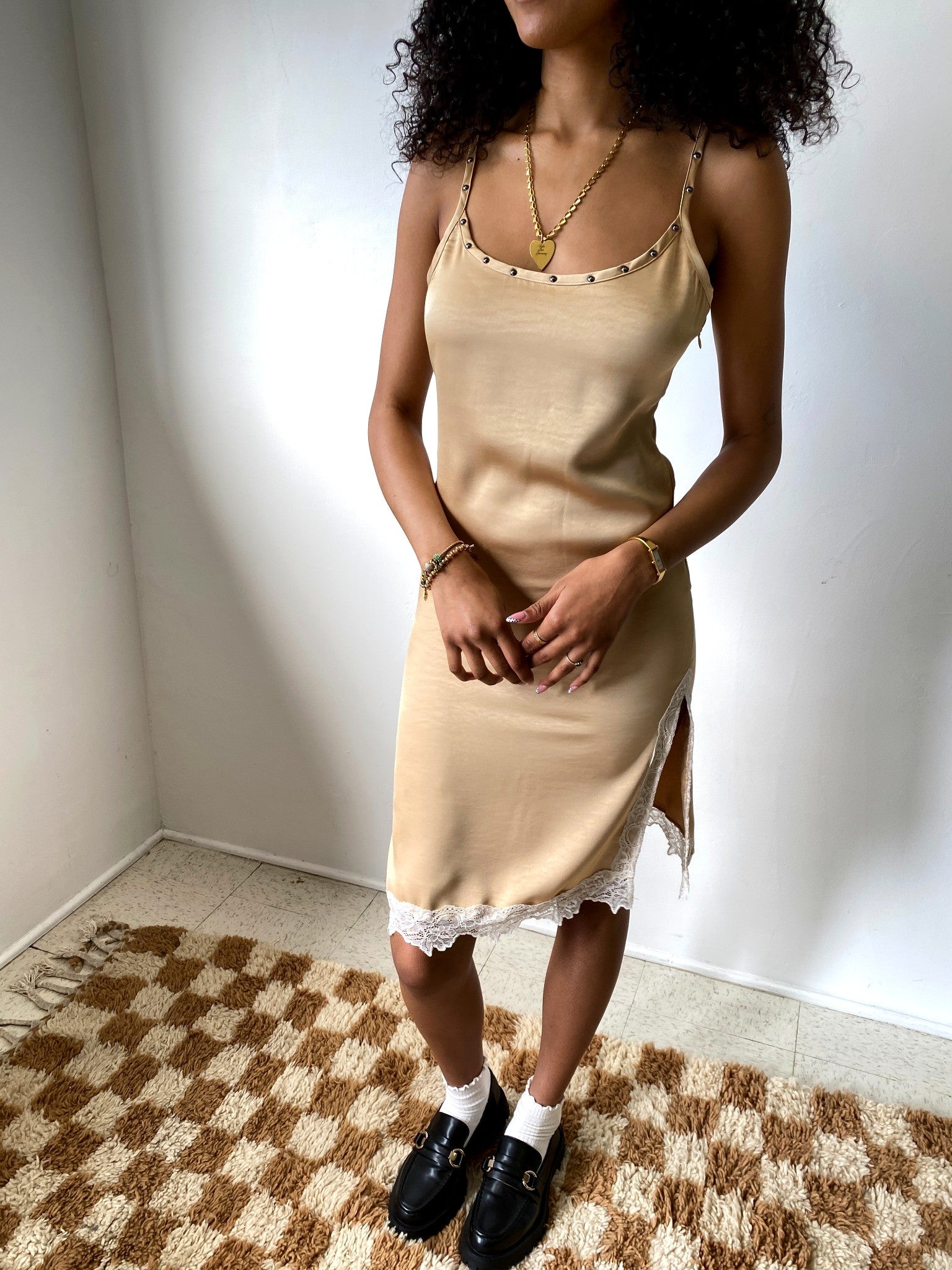 Woman wearing a beige slip dress with lace trim in a room with a checkered floor.