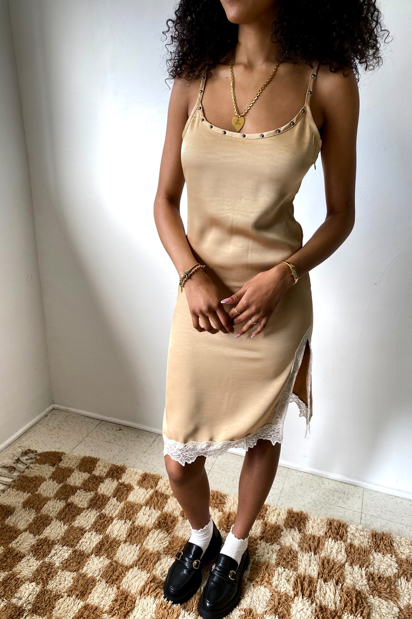 Woman wearing a beige slip dress with lace trim on a checkered floor.