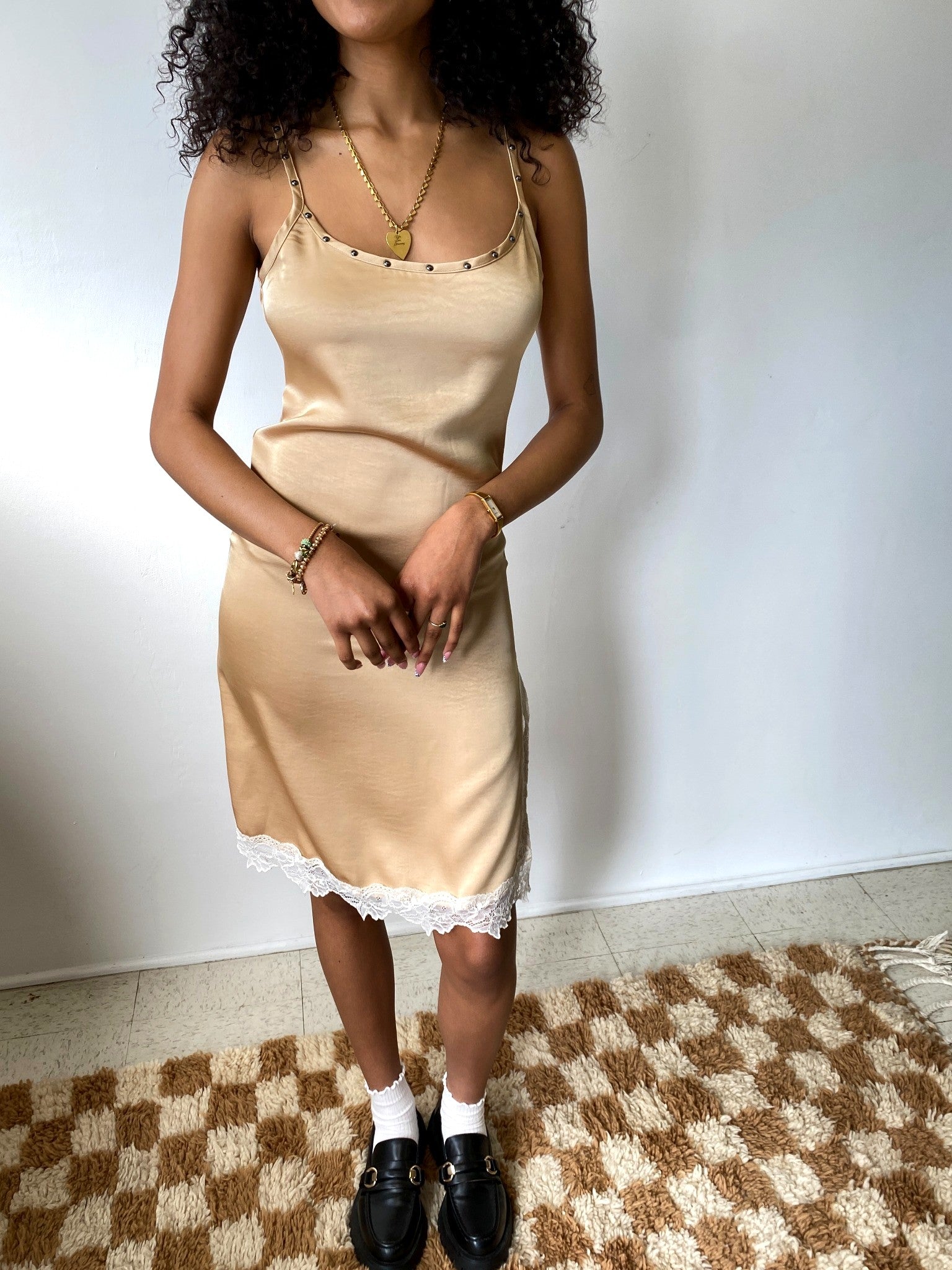 Woman wearing a beige slip dress standing on a checkered rug.