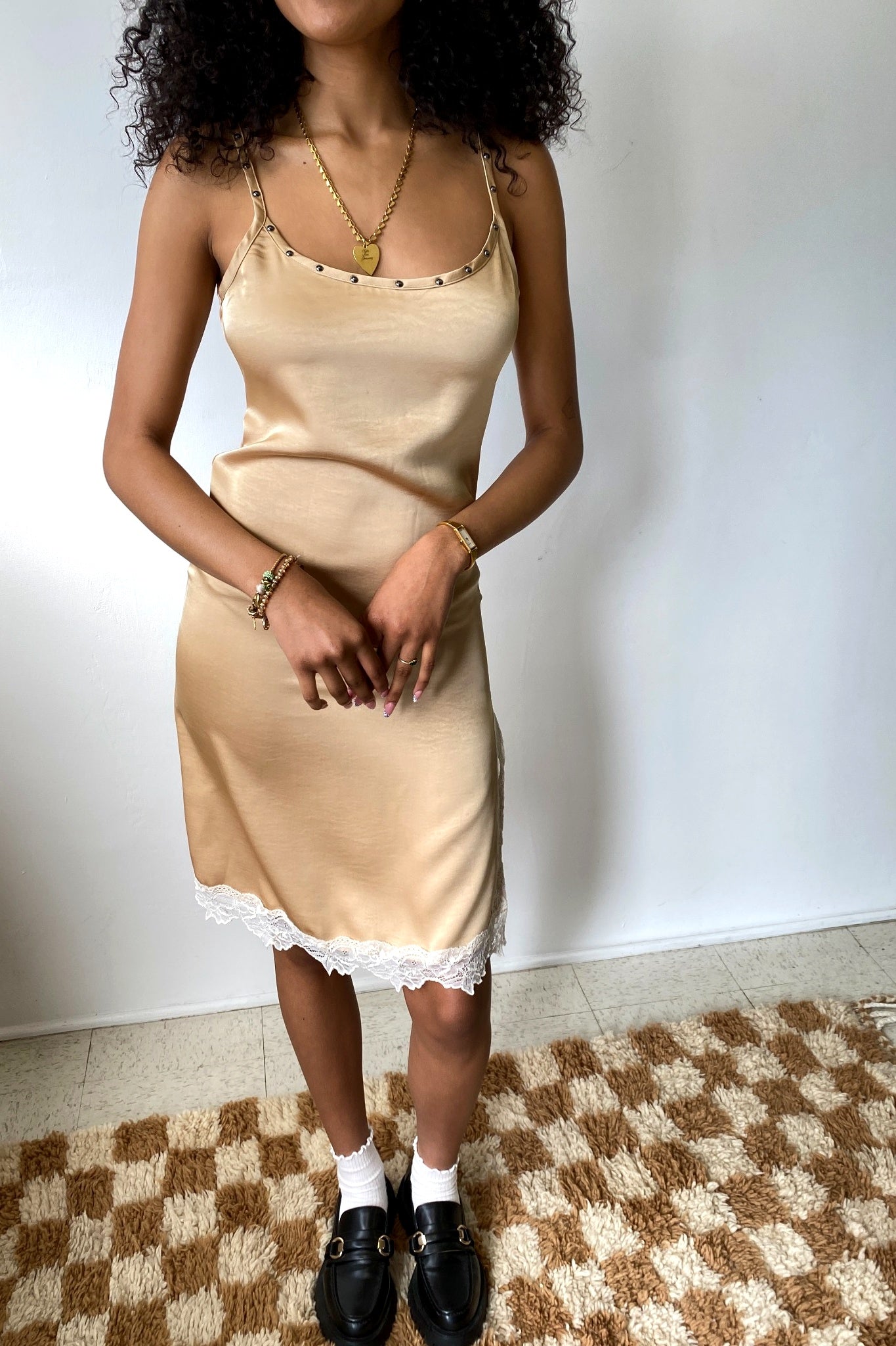 Woman wearing a beige slip dress with lace trim on a checkered floor.