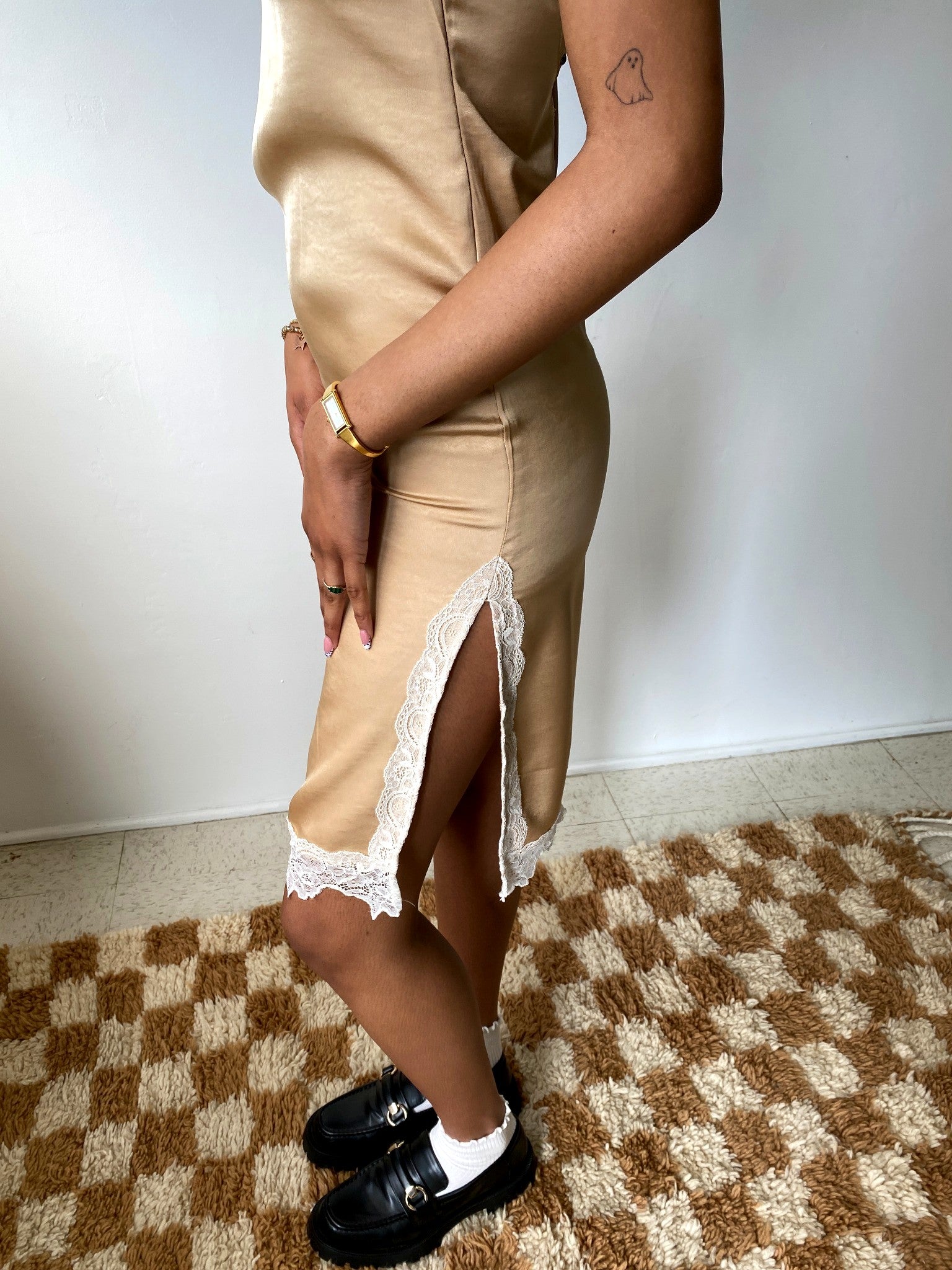 Person wearing a beige dress with lace trim on a checkered floor.