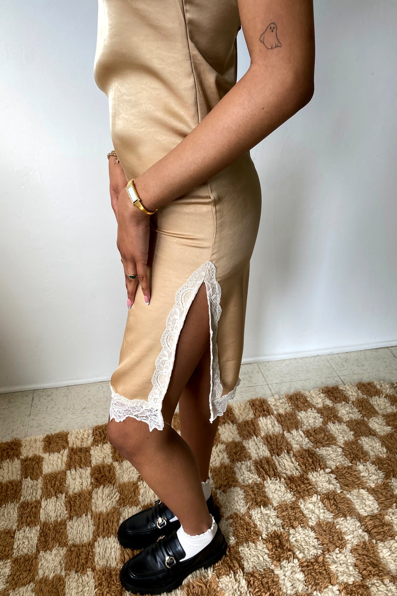 Person wearing a beige dress with lace trim on a checkered floor.