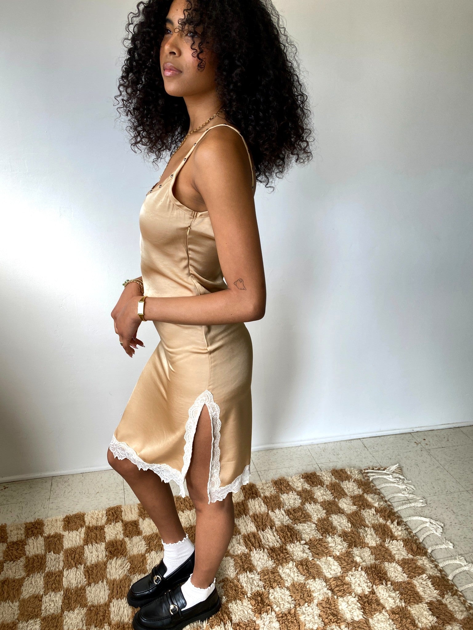 Woman wearing a beige satin slip dress with lace trim on a checkered rug.