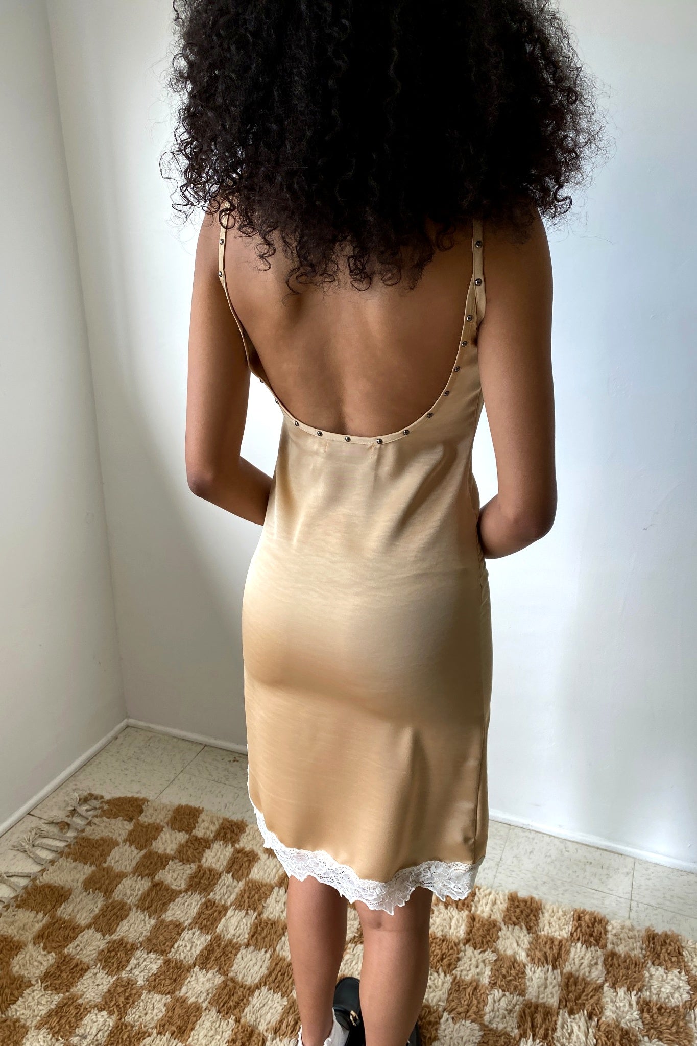 Woman wearing a beige slip dress with lace trim in a room with a checkered floor.