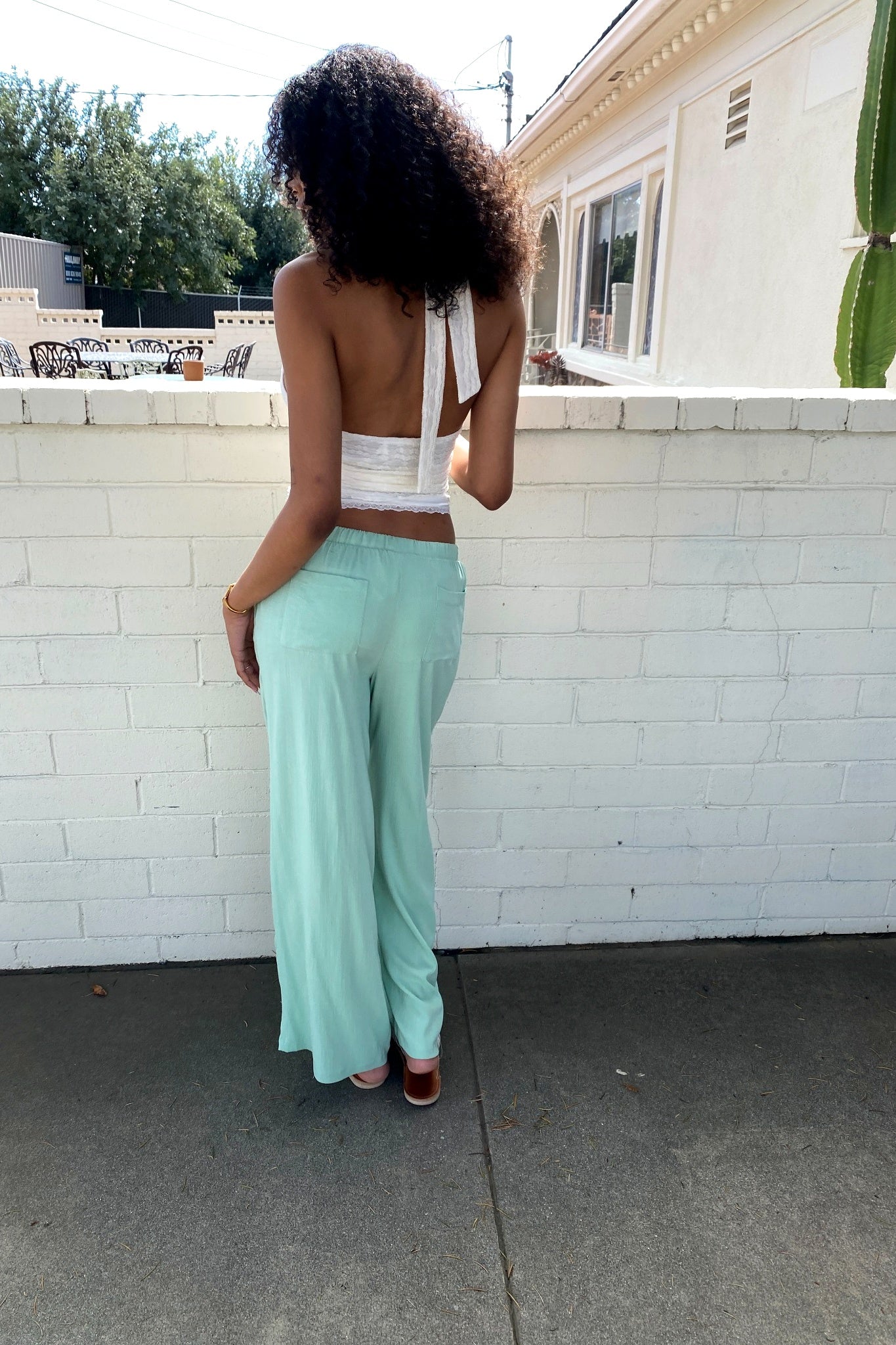 Person wearing a white top and light green pants standing in front of a white brick wall.
