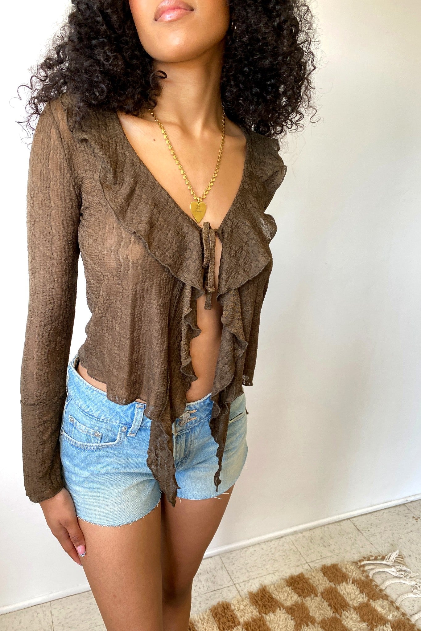 Woman wearing a brown cardigan over a top and denim shorts against a plain background