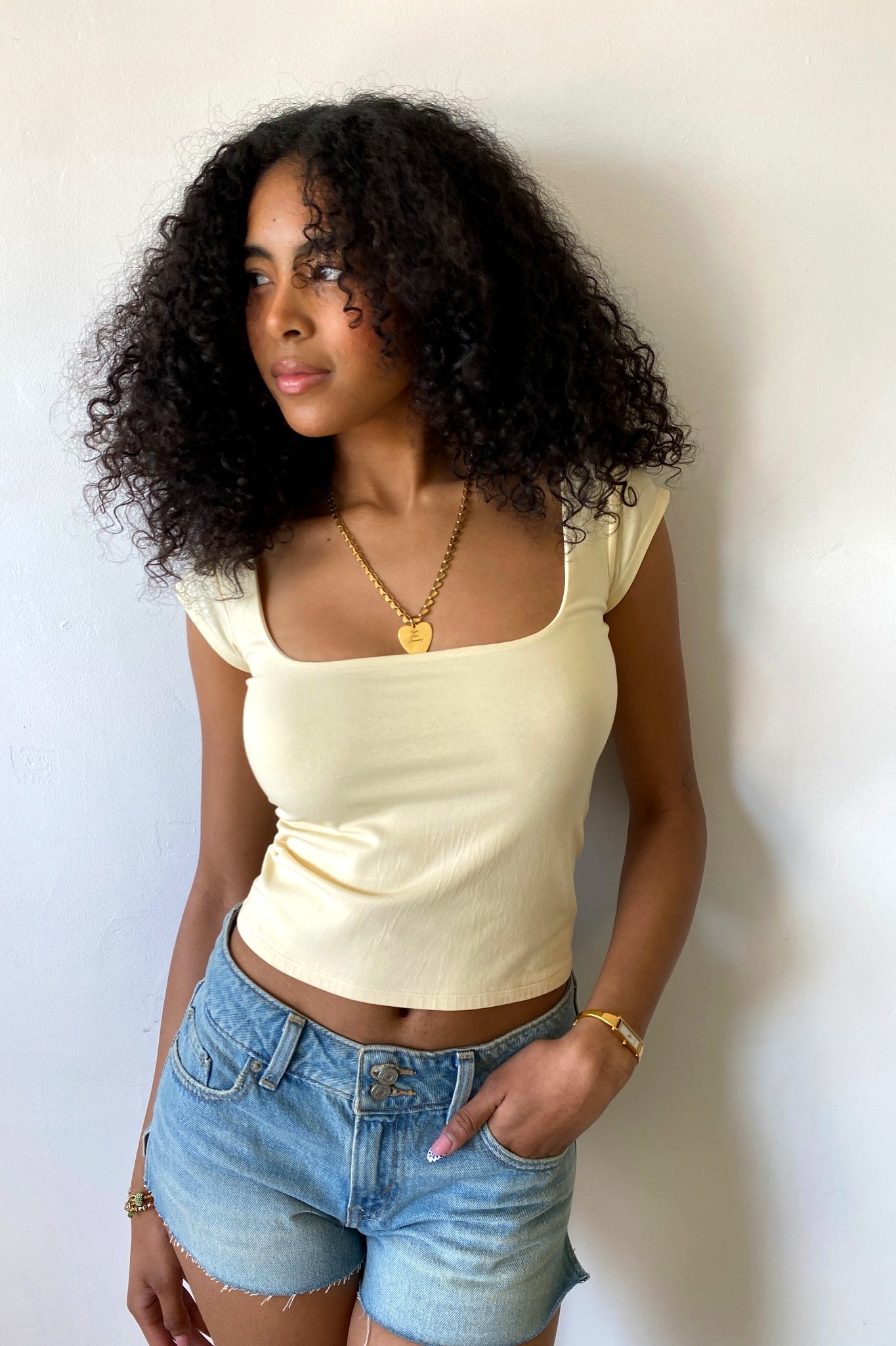Woman wearing a light yellow top and denim shorts against a plain background