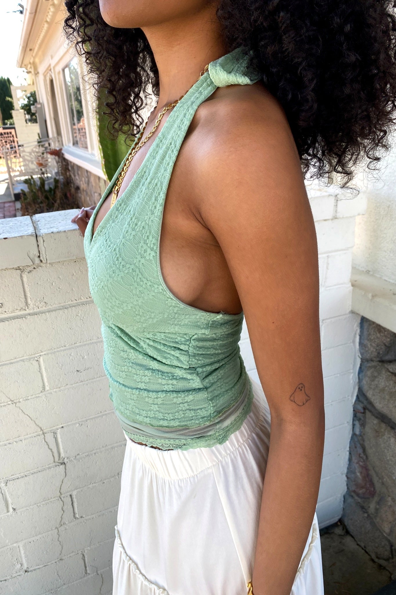 Woman wearing a green top and white skirt standing outdoors.