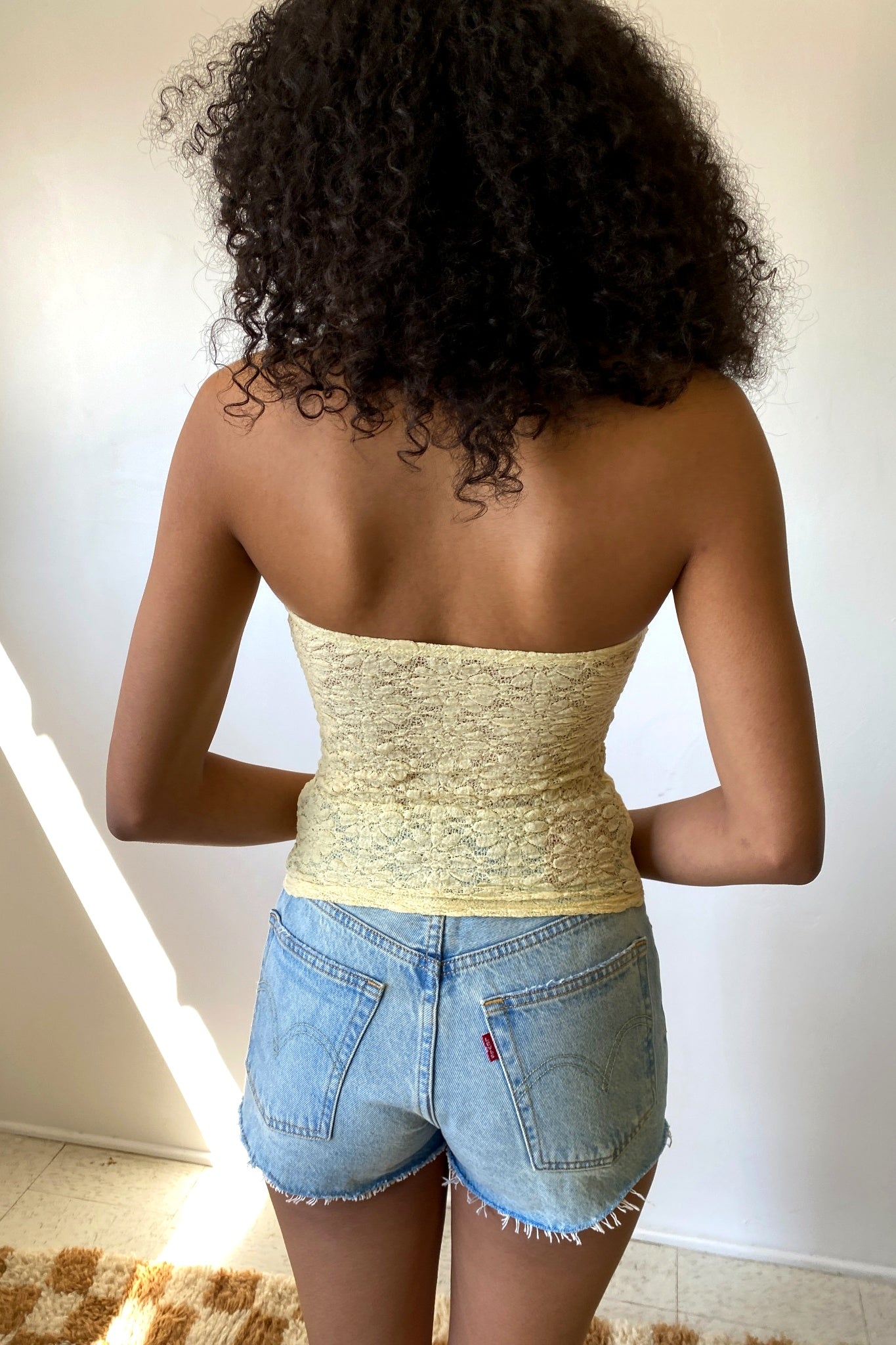 Person wearing a strapless top and denim shorts with a neutral background