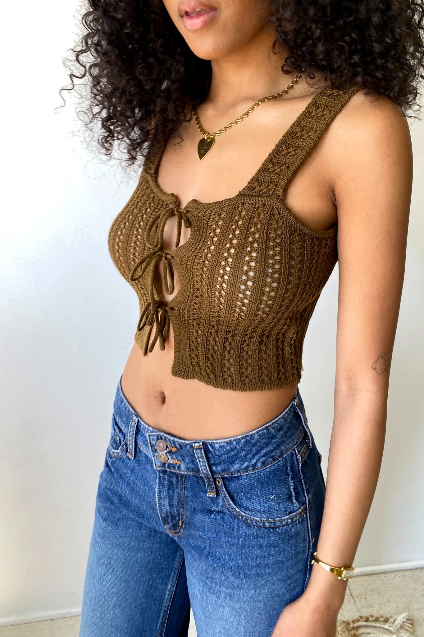 Woman wearing a brown crochet top and blue jeans against a white background