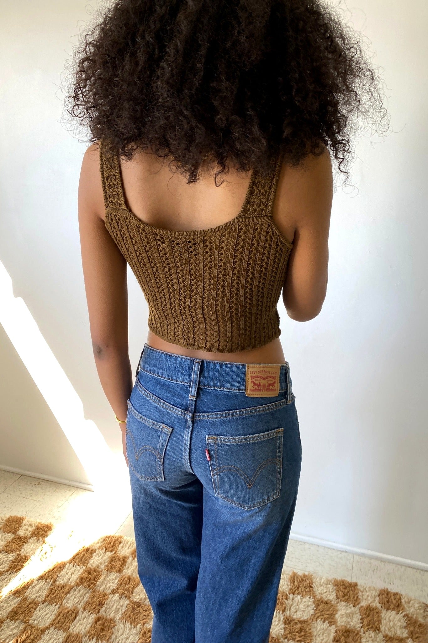 Person wearing a brown crochet top and blue jeans indoors.