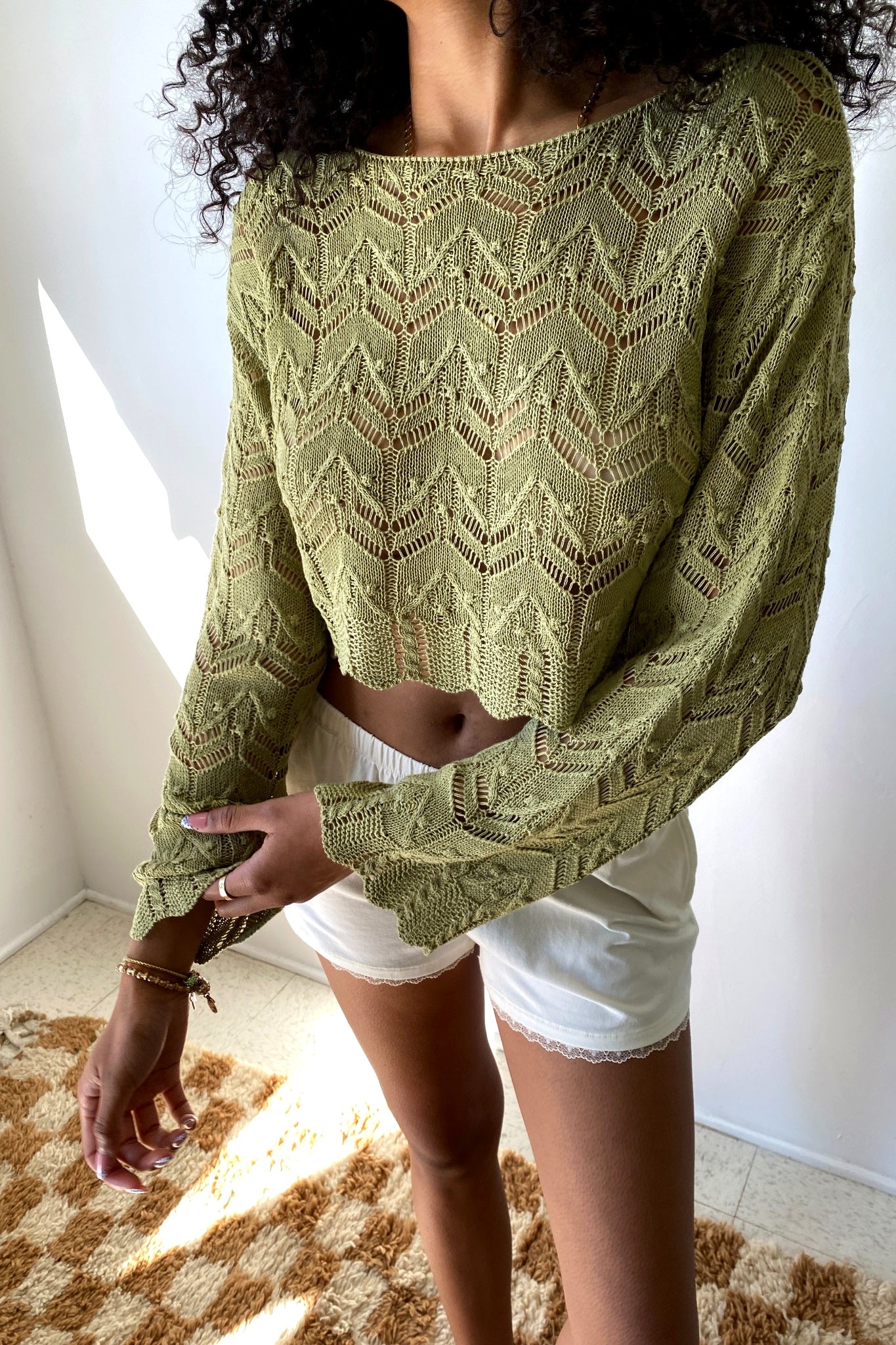 Person wearing a green patterned sweater and white shorts indoors.