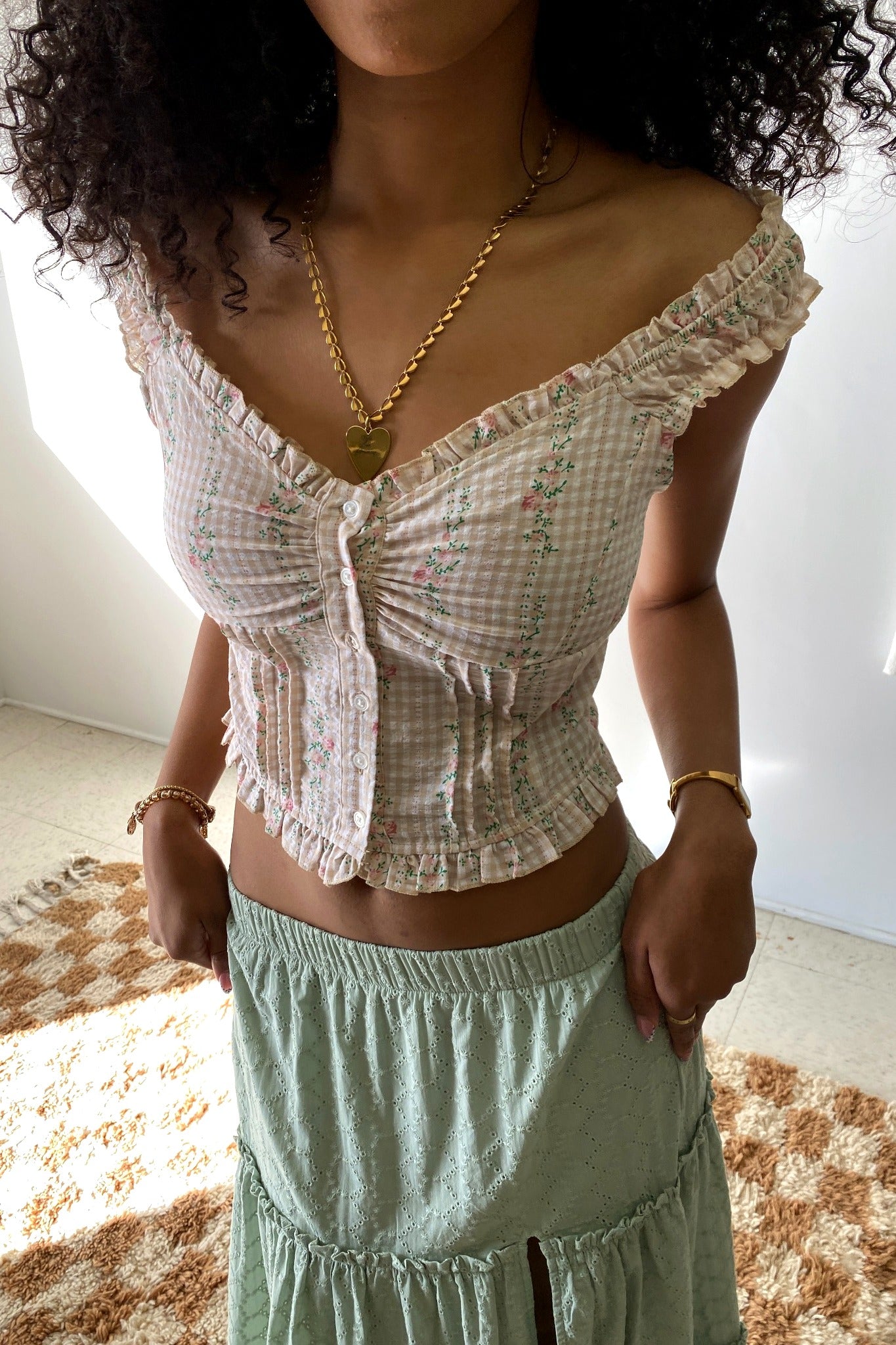 Woman wearing a white checkered top and green skirt with a gold necklace.
