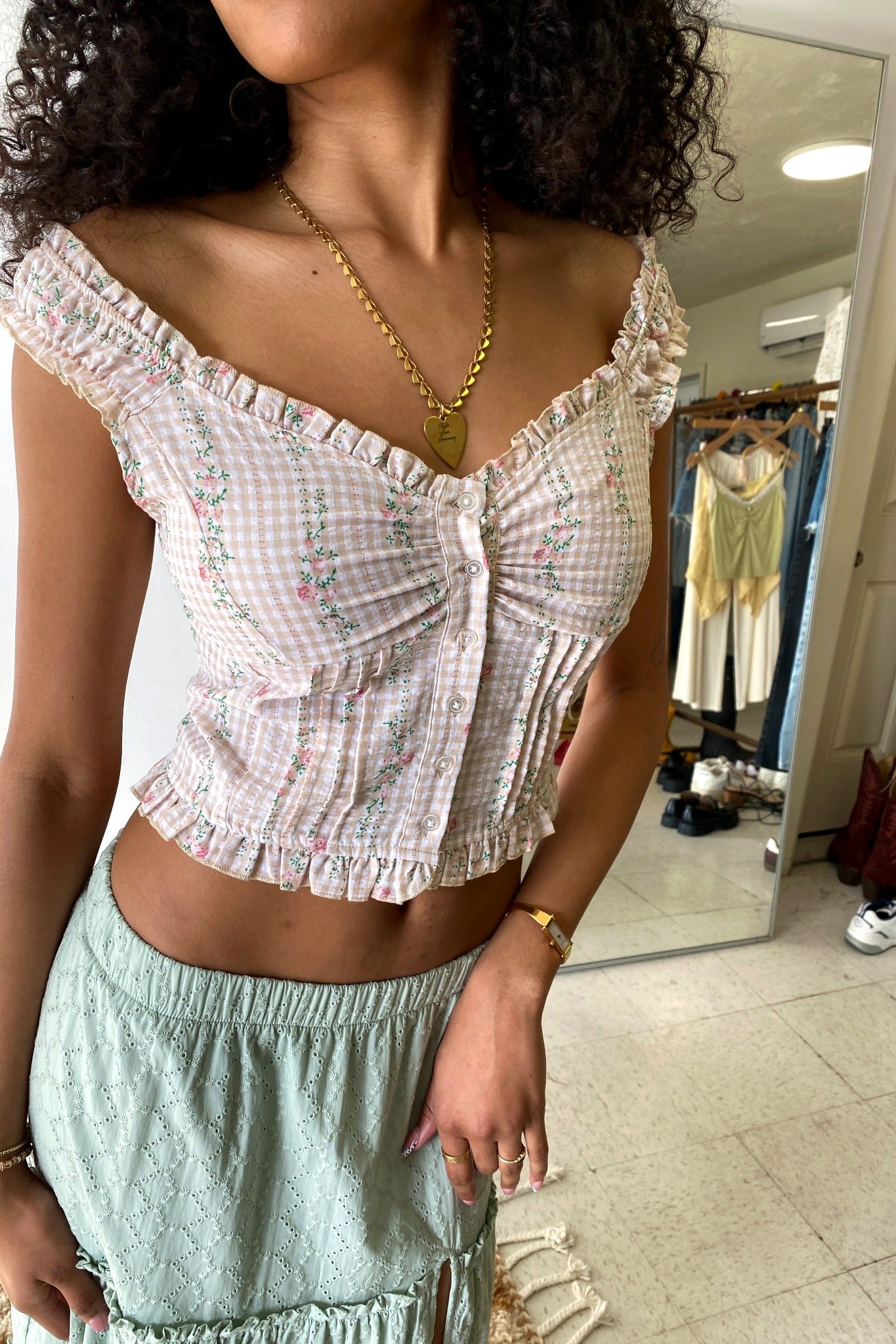 Woman wearing a white checkered top and light blue shorts in a room with a mirror.