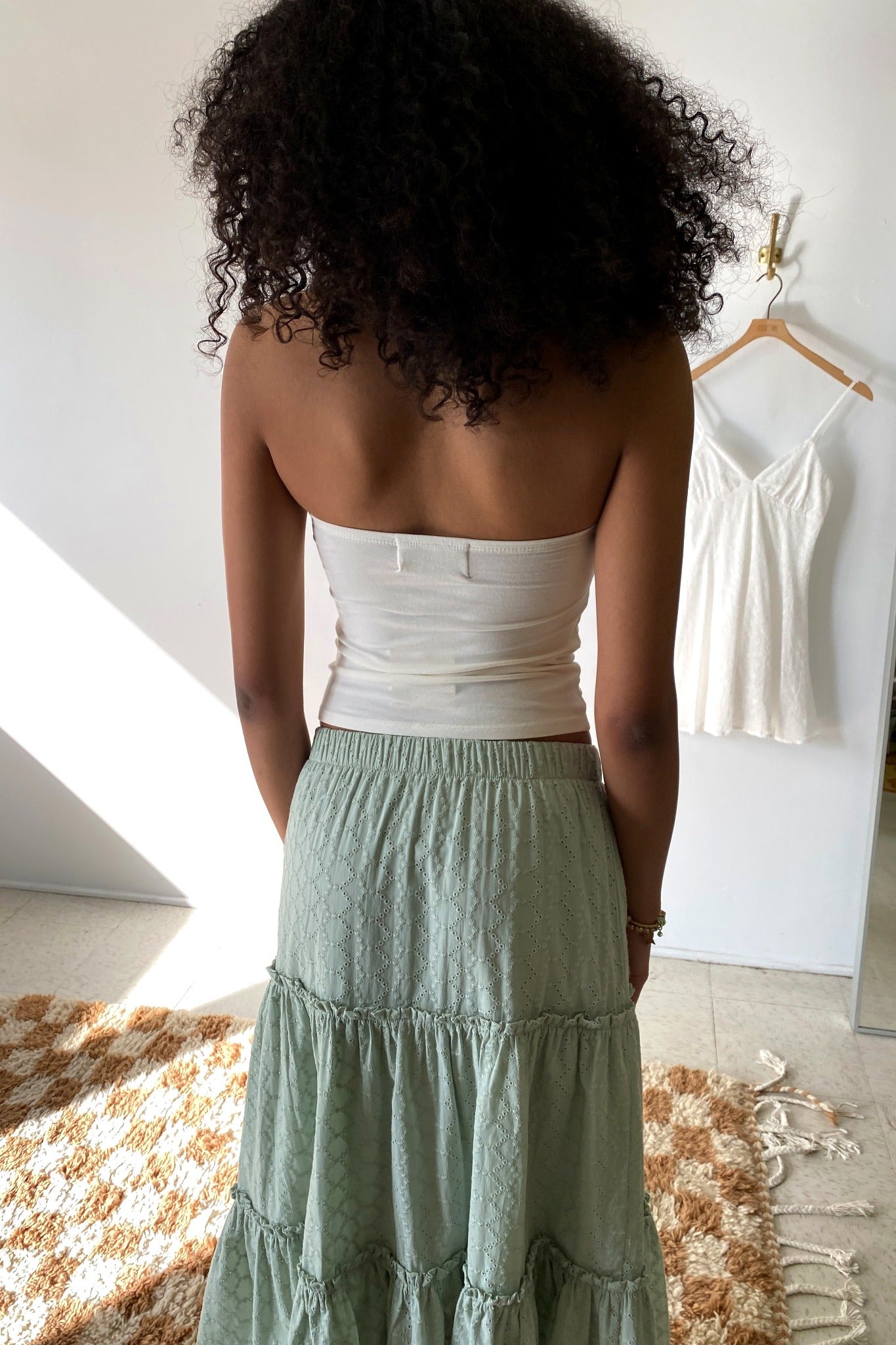 Woman wearing a white top and green skirt in a room with a white wall and wooden floor.