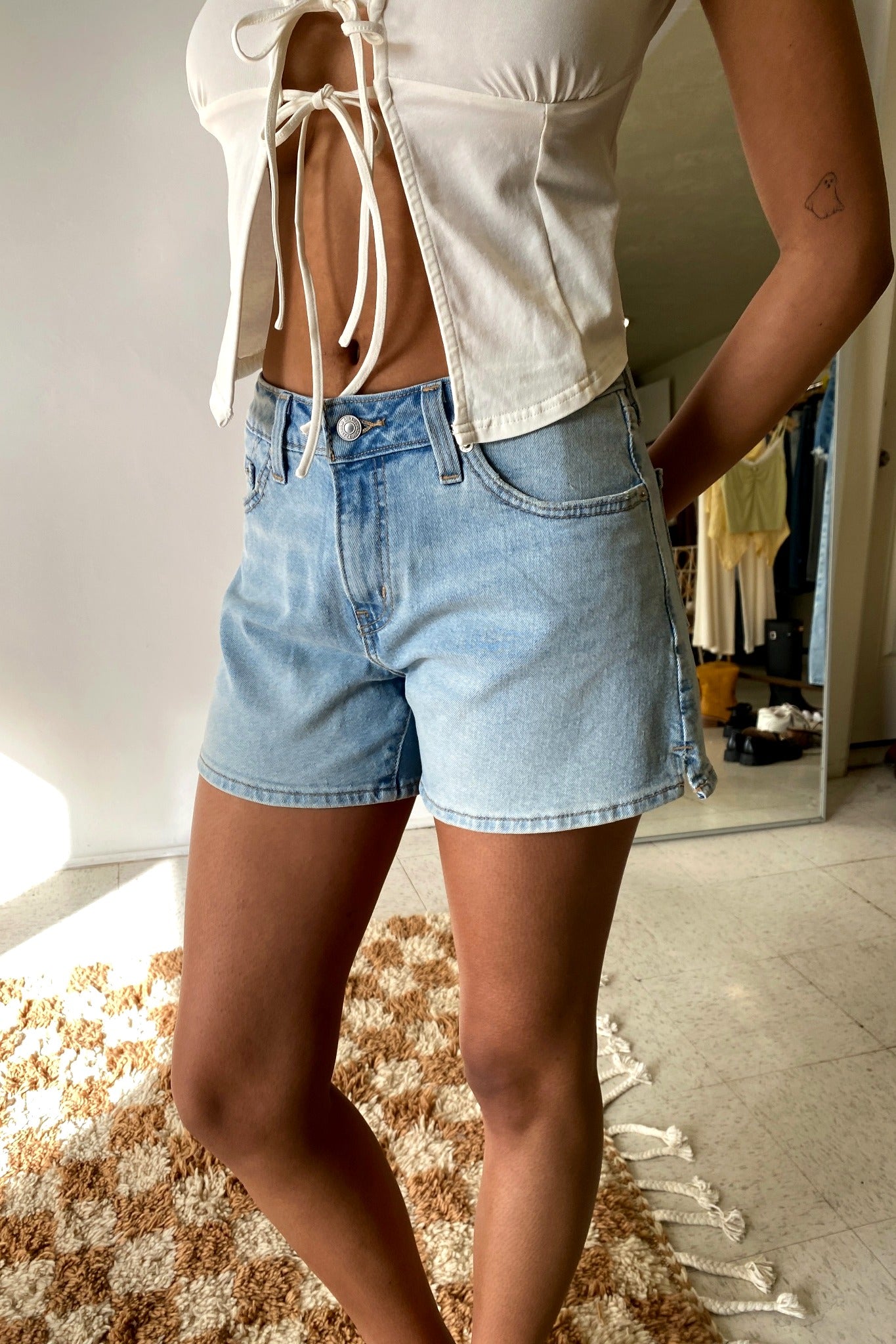 Person wearing light blue denim shorts and a cream-colored top in a room.