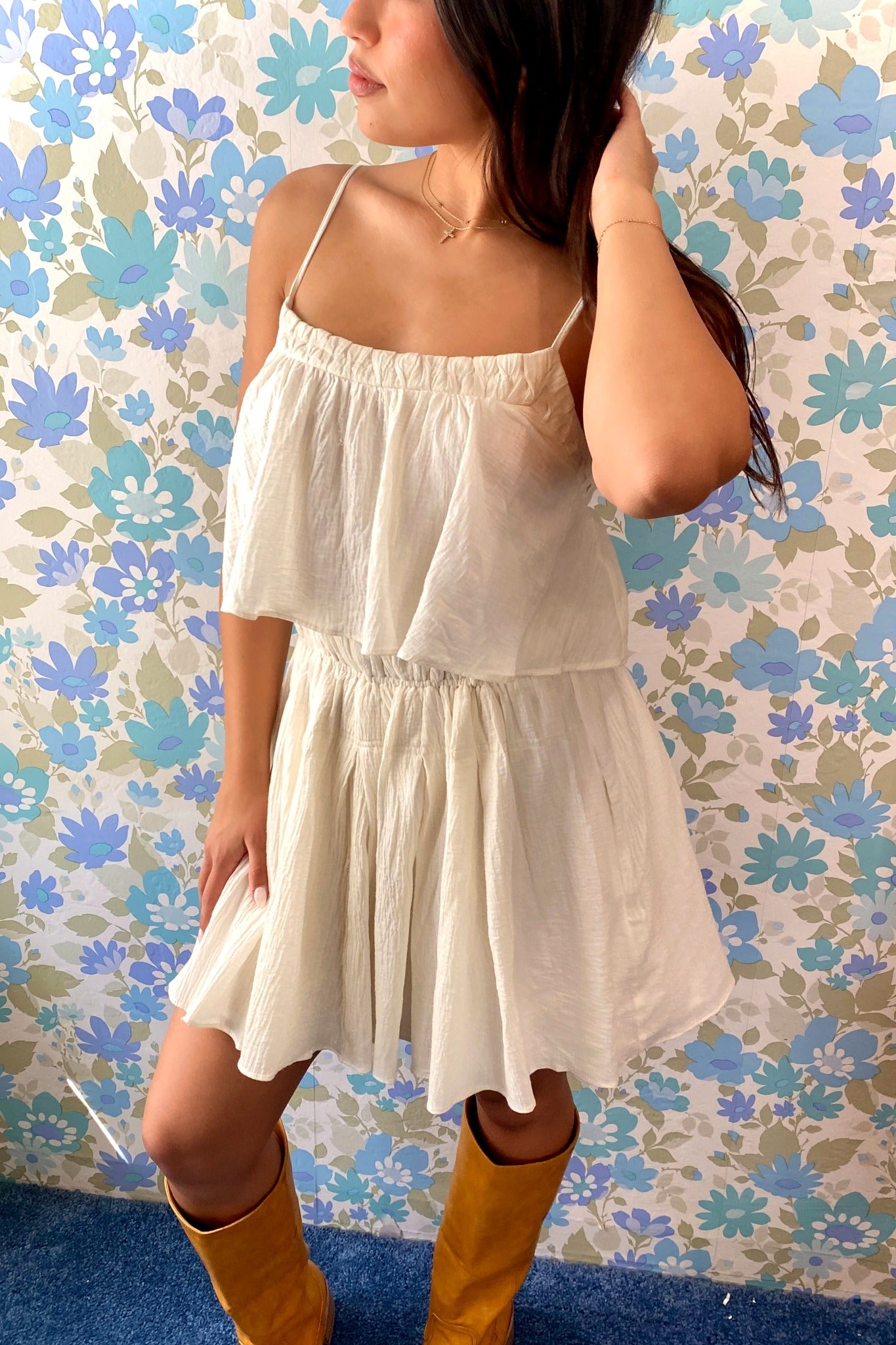Woman wearing a white dress and yellow boots against a floral wallpaper background