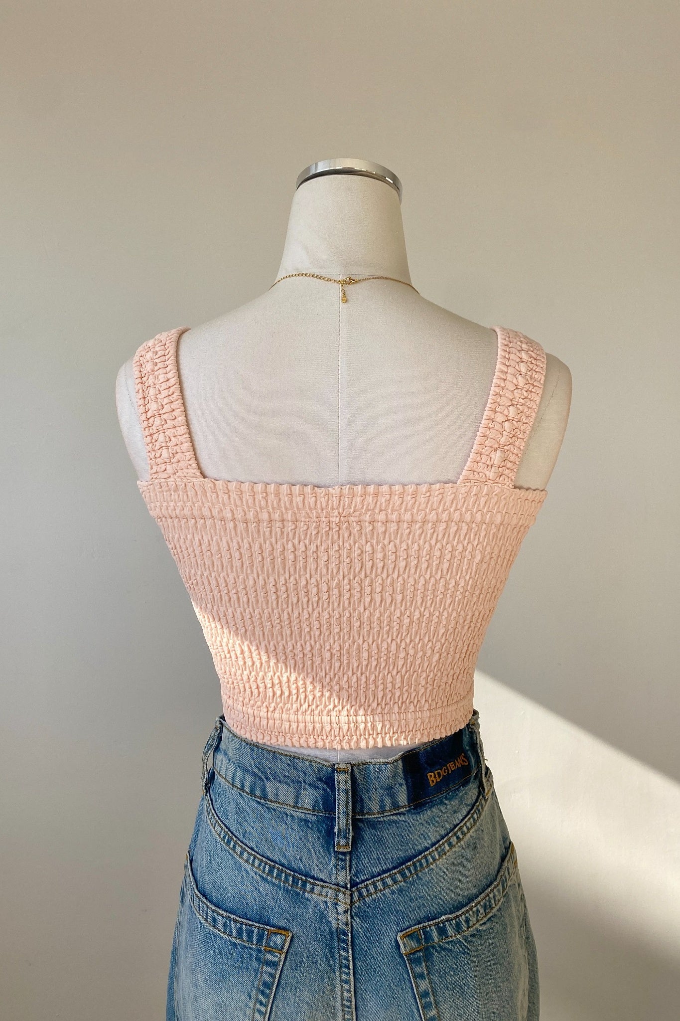 Mannequin wearing a light pink textured top and blue jeans against a neutral background
