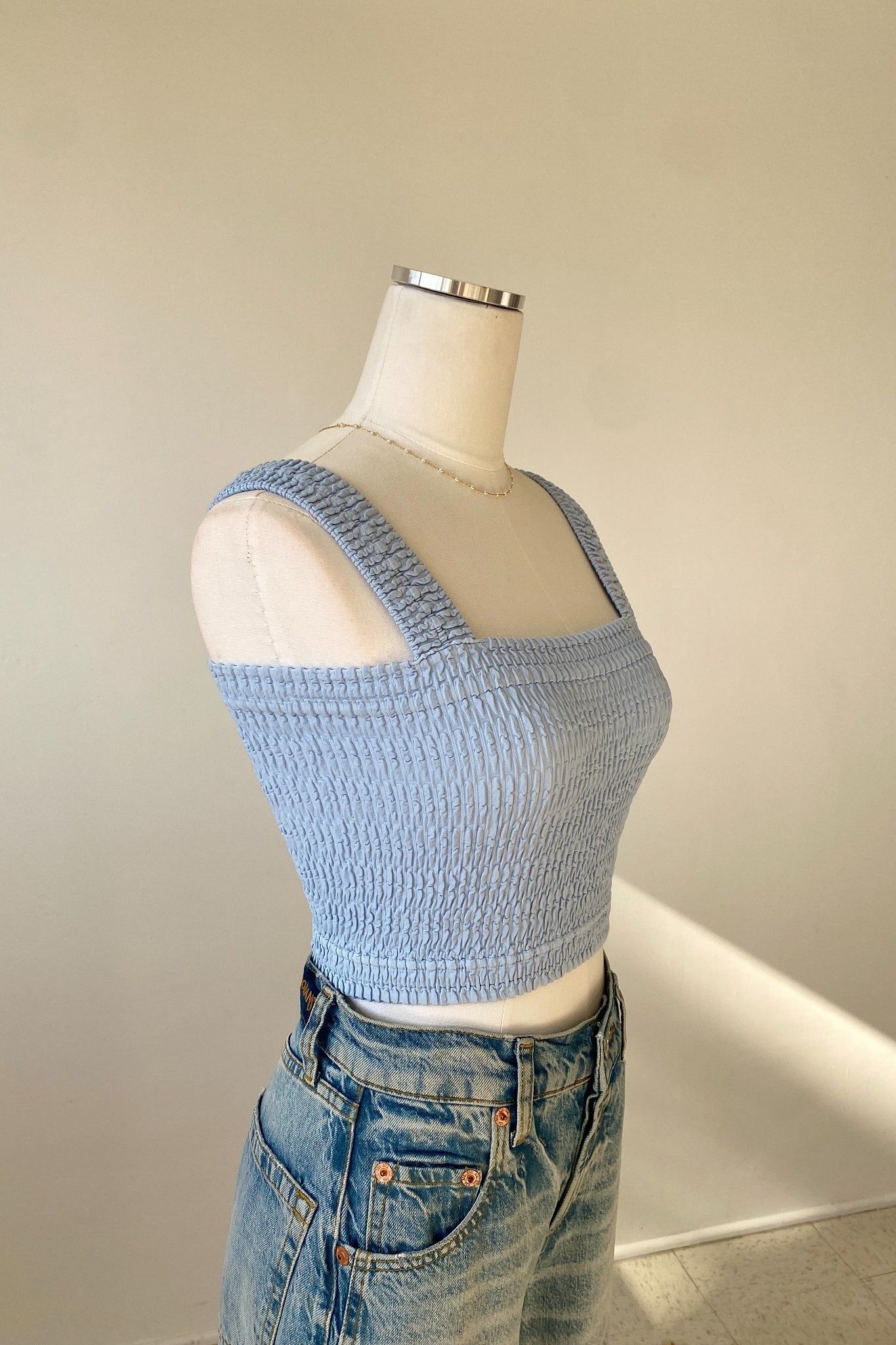 Light blue knitted crop top on a mannequin with jeans against a neutral background
