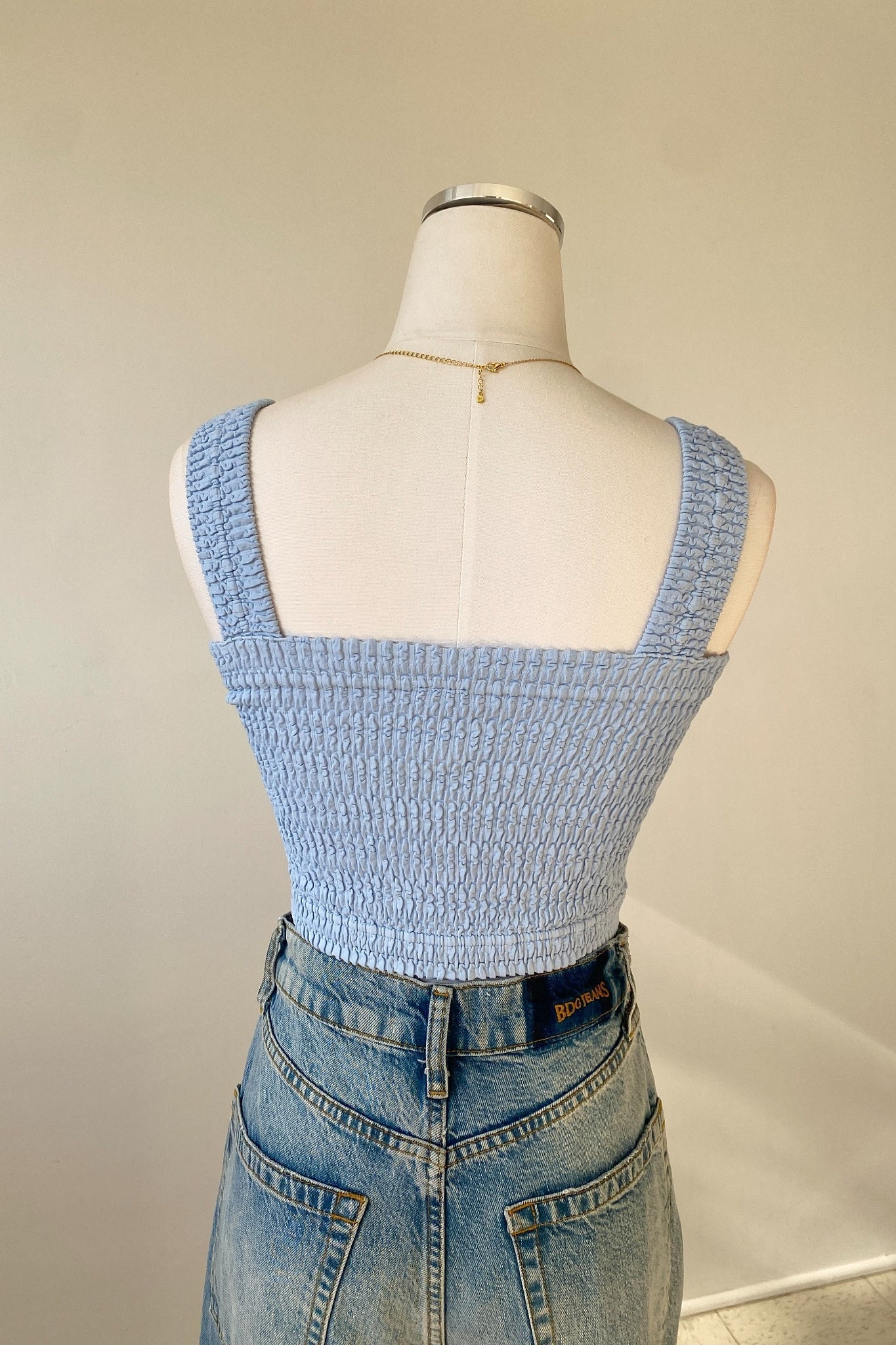Mannequin wearing a light blue smocked top and jeans against a plain background
