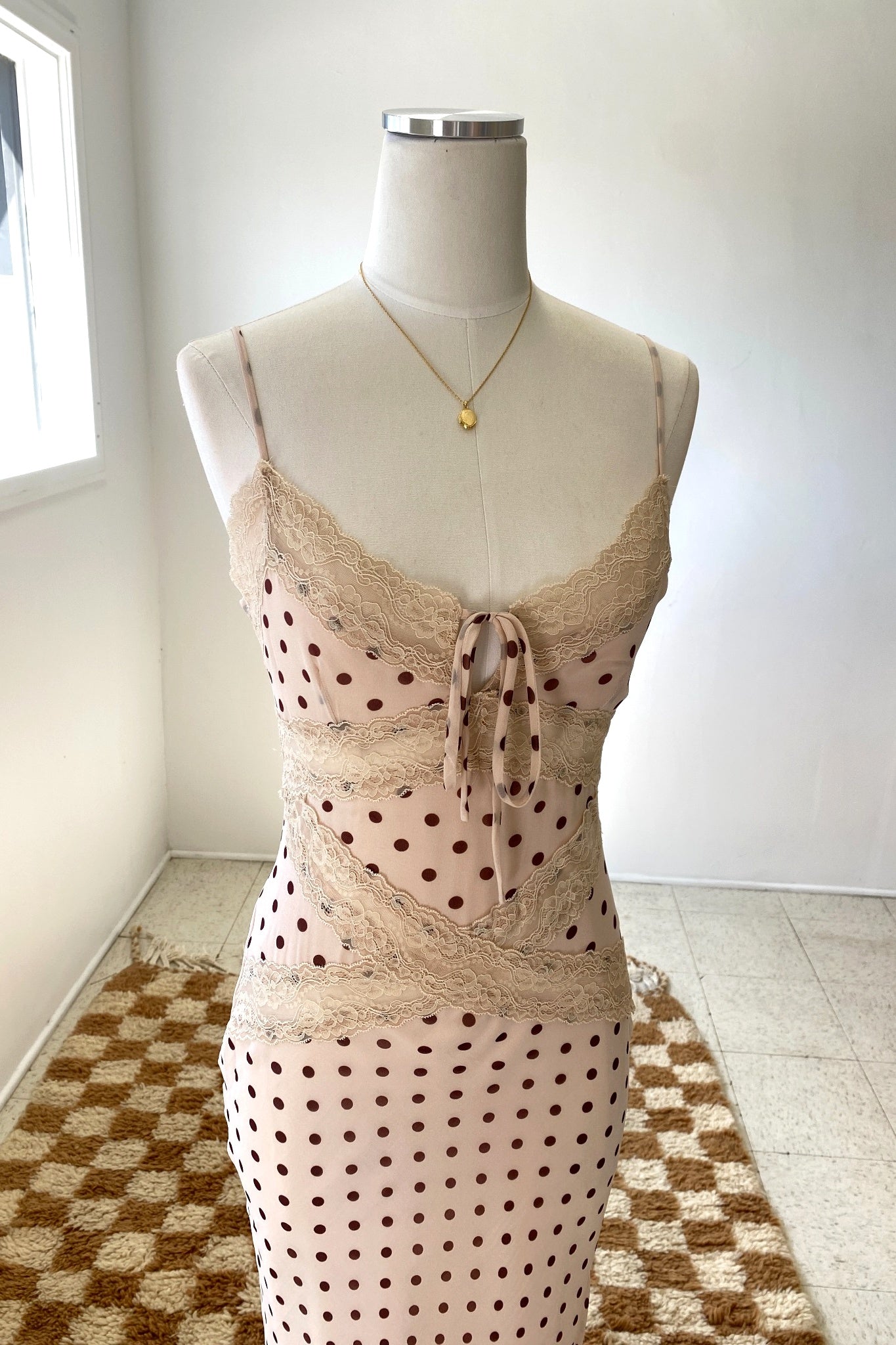 Mannequin wearing a beige lace top and polka dot pants on a checkered floor.