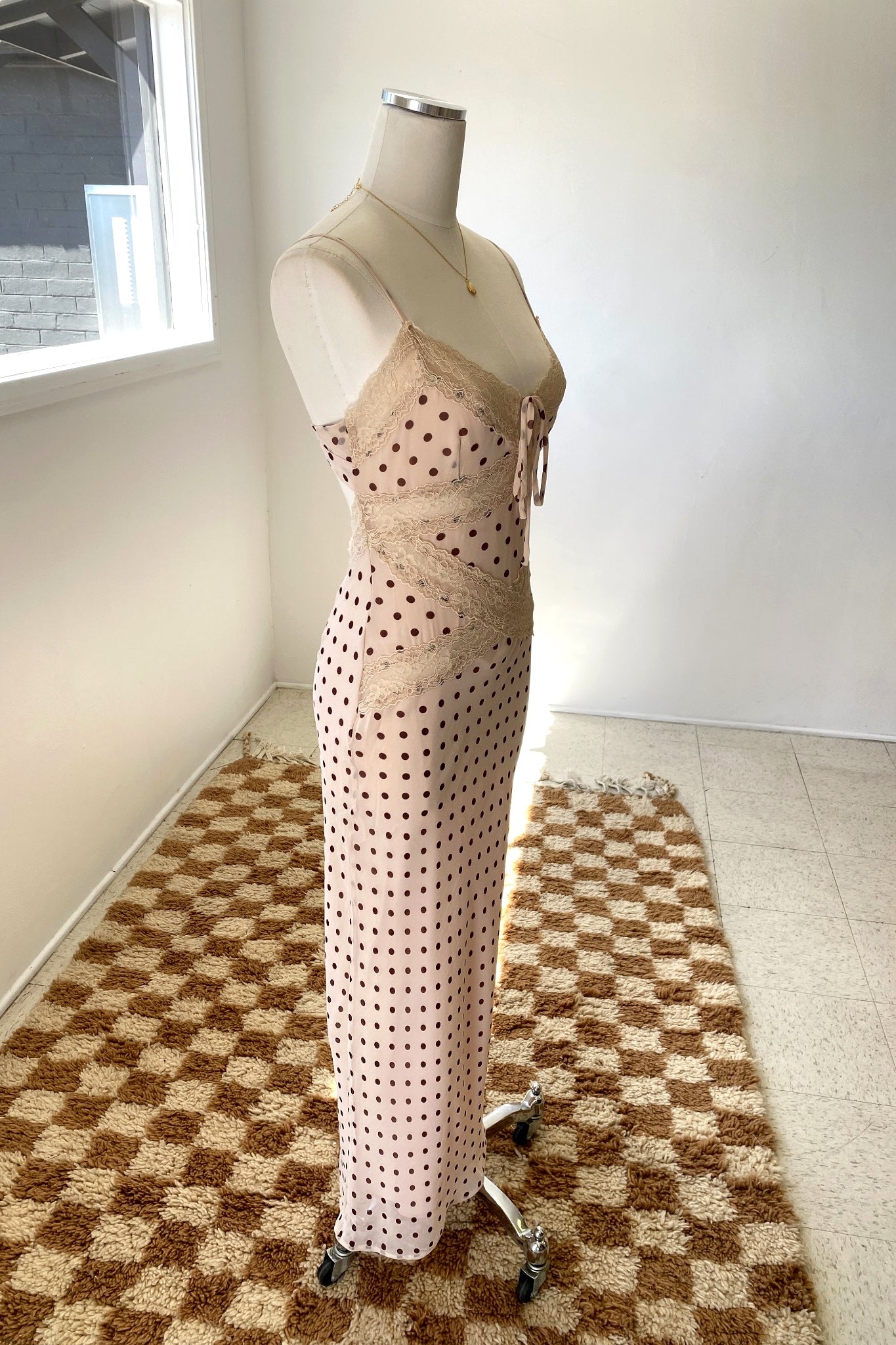 Mannequin wearing a beige dress with black polka dots on a checkered floor.