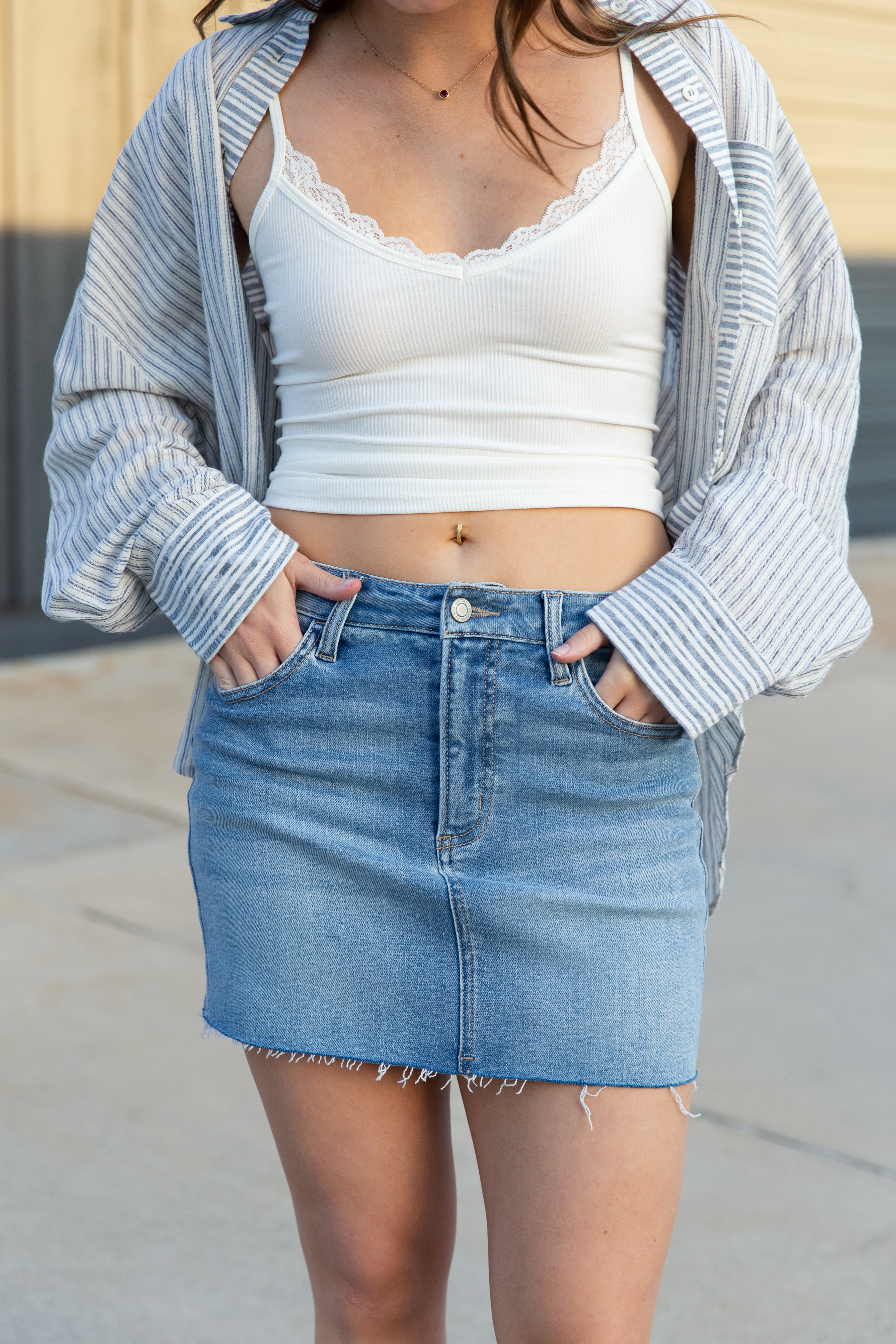 Person wearing a white crop top and blue denim skirt with a striped shirt over shoulders.
