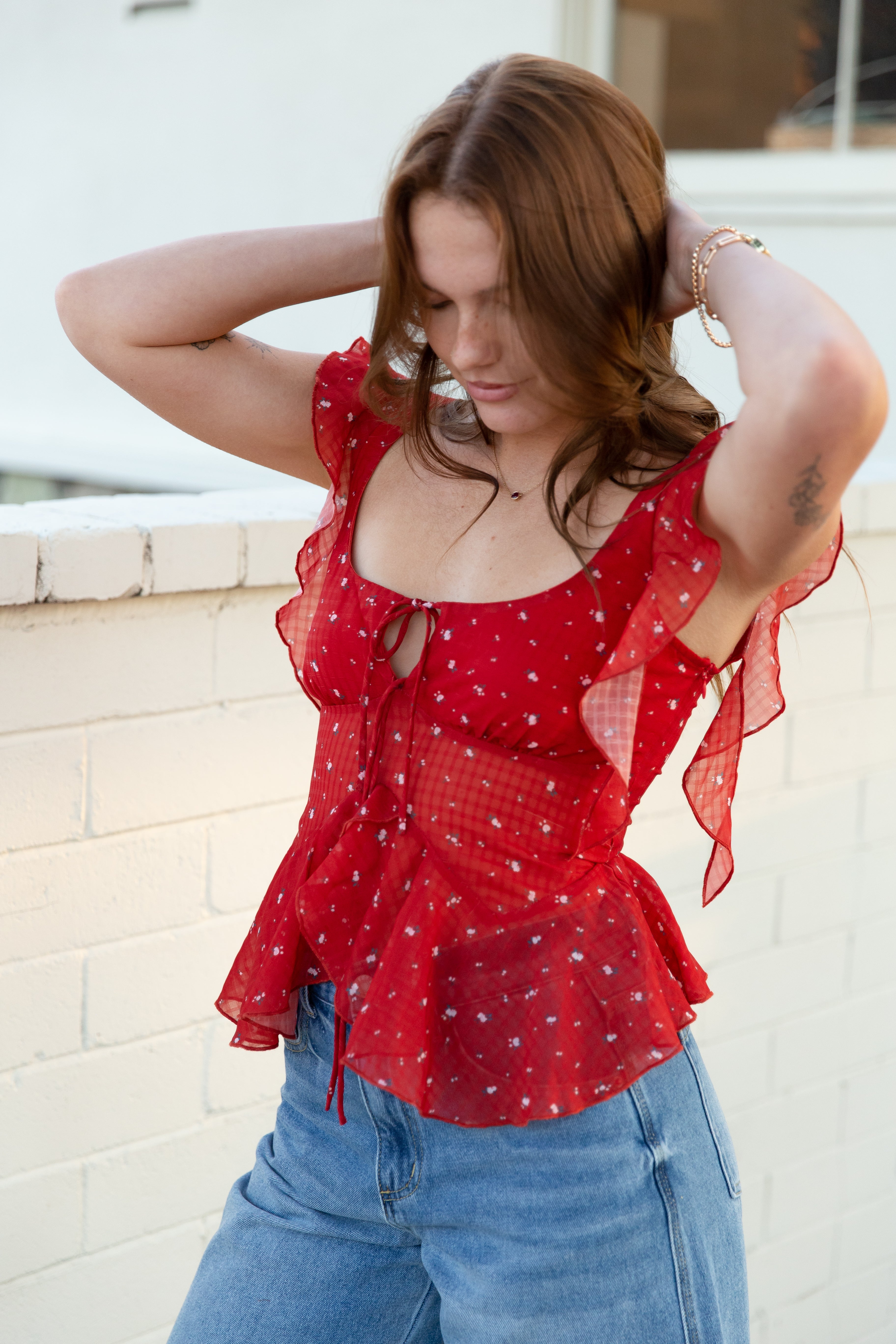 Woman wearing a red polka dot blouse and blue jeans against a white wall.