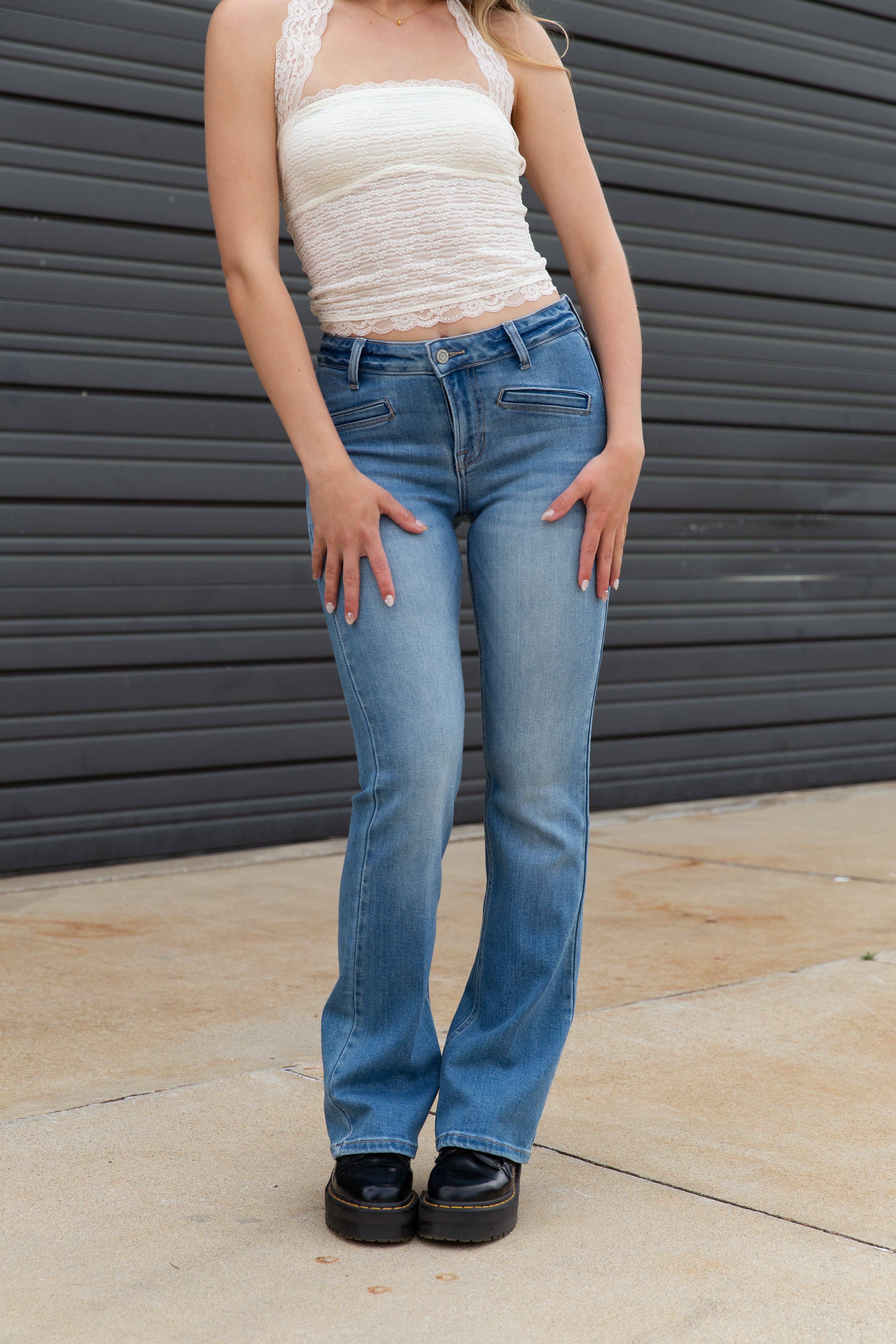 Person wearing a white top and blue jeans standing against a dark gray wall.