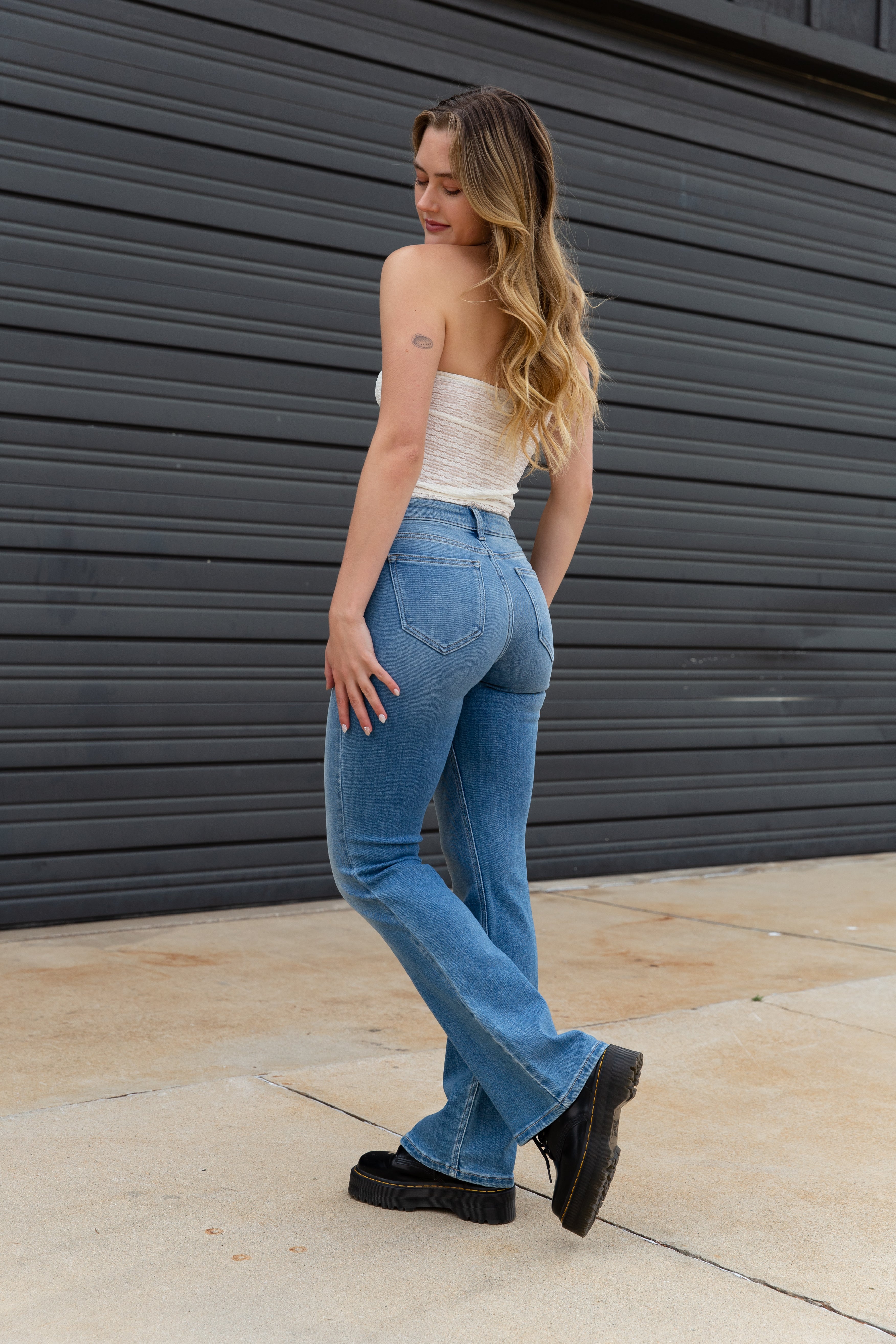 Woman wearing a white top and blue jeans standing against a dark gray wall.