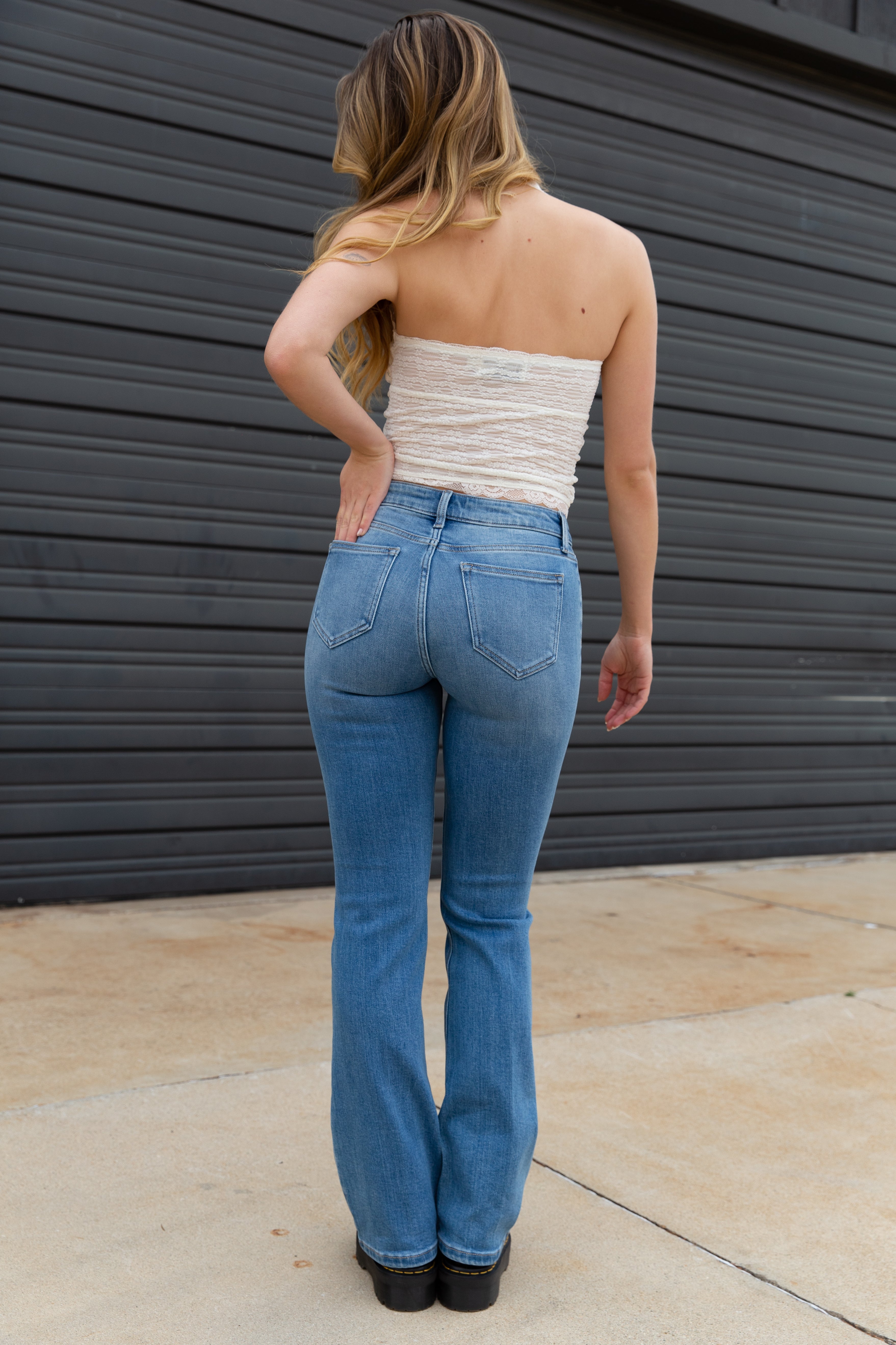 Woman wearing a strapless top and blue jeans standing in front of a gray wall.