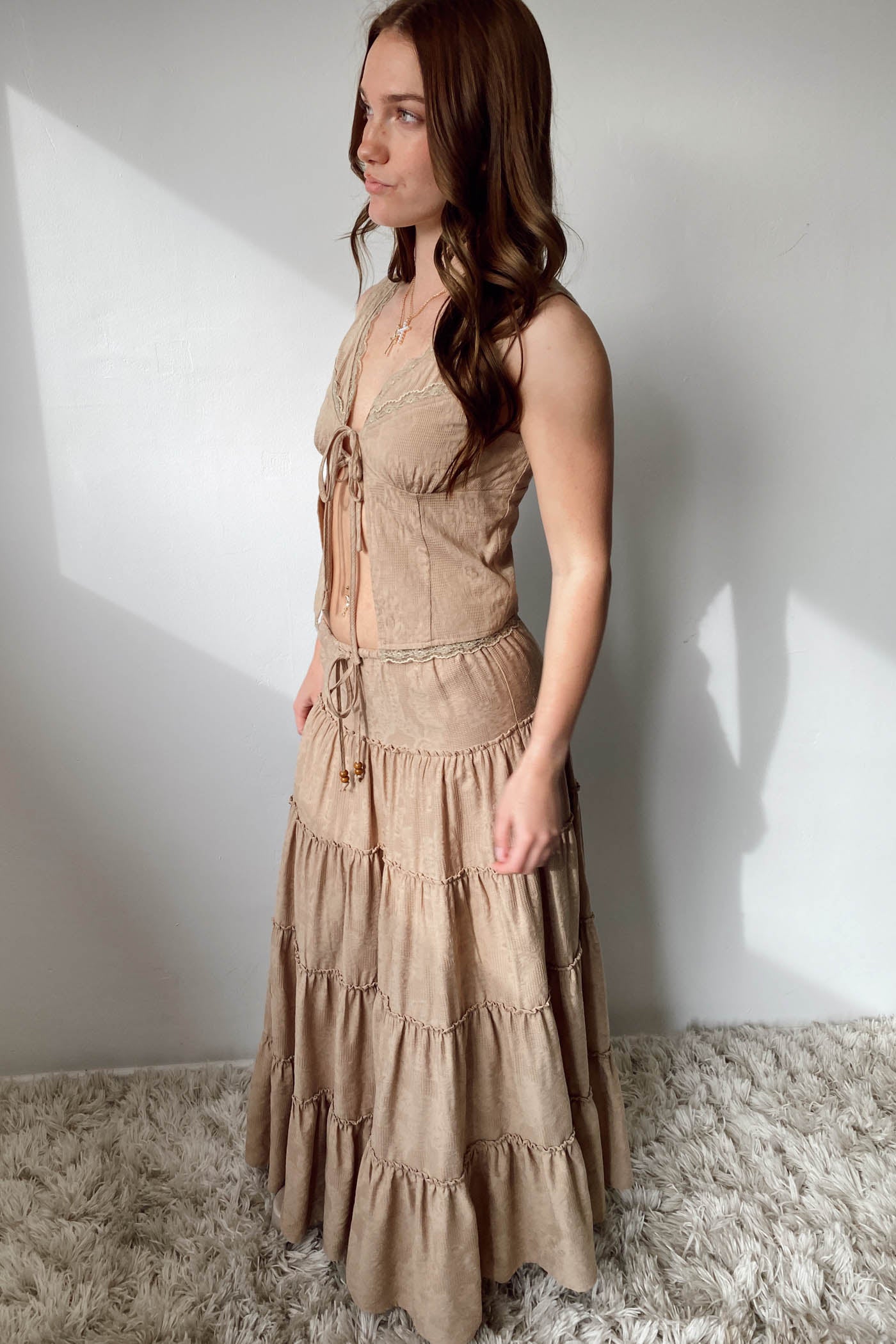 Woman wearing a beige dress standing against a white wall.