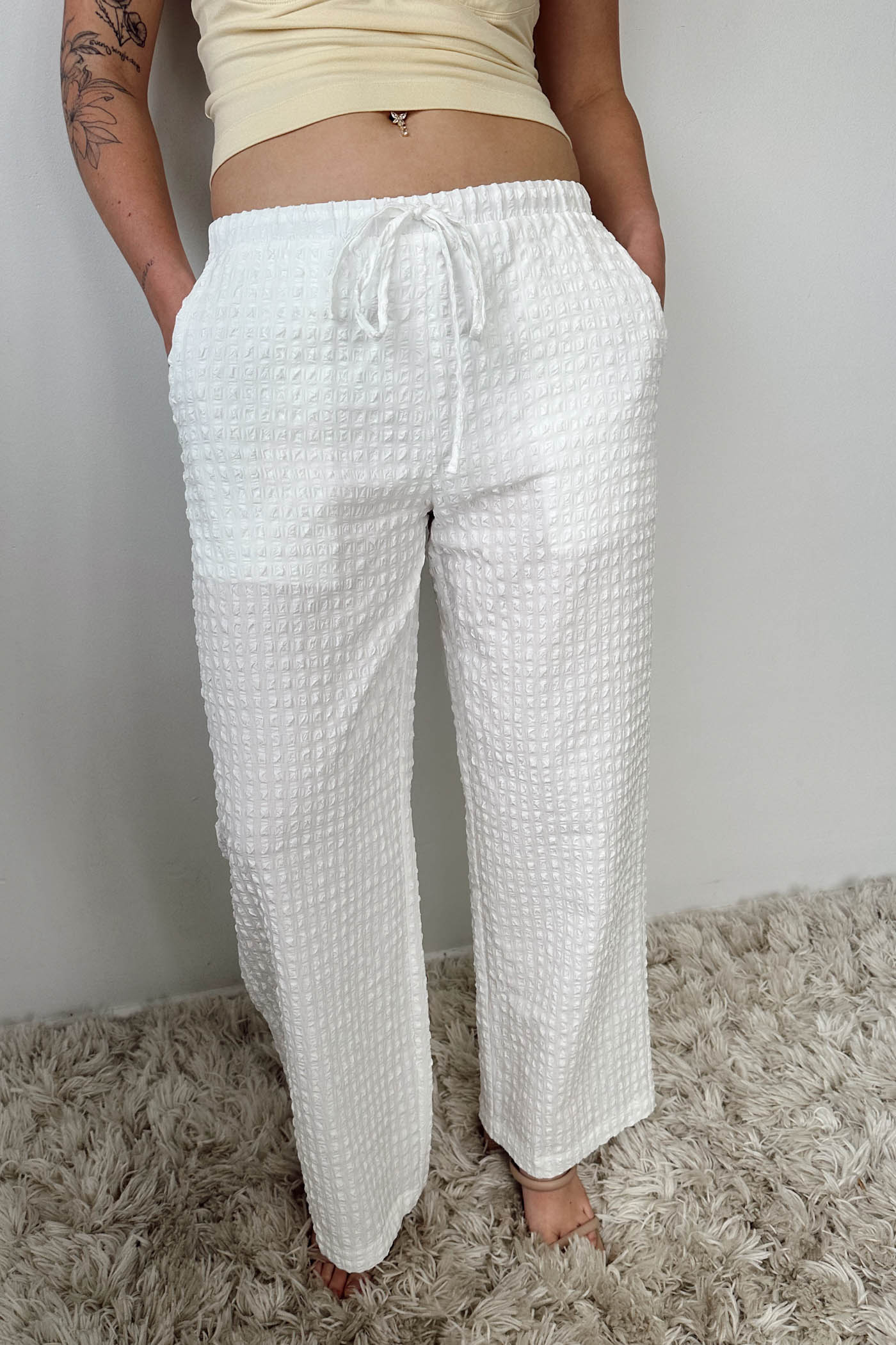 Person wearing white textured pants on a neutral background