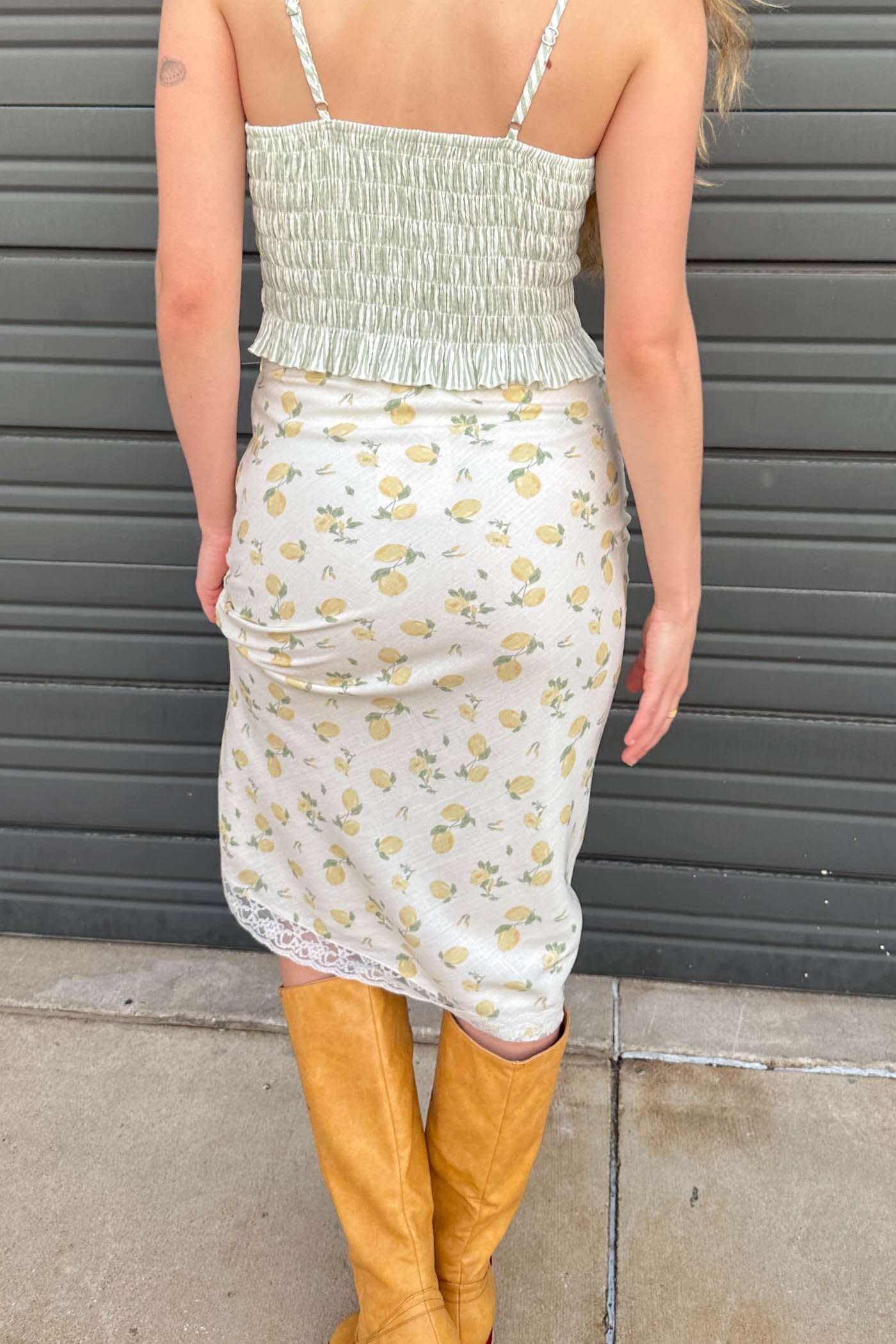 Person wearing a floral dress with a smocked top and yellow knee-high boots against a gray background.