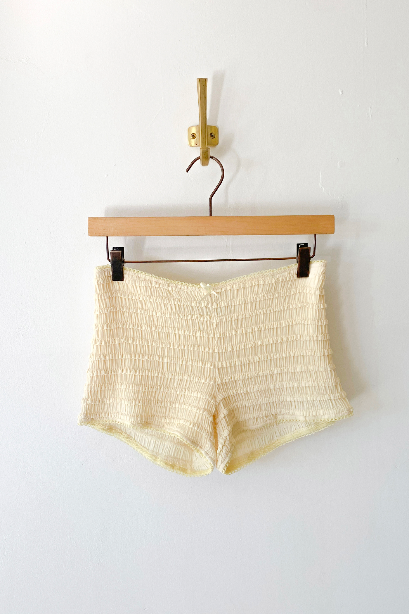 Yellow shorts on a wooden hanger against a white wall