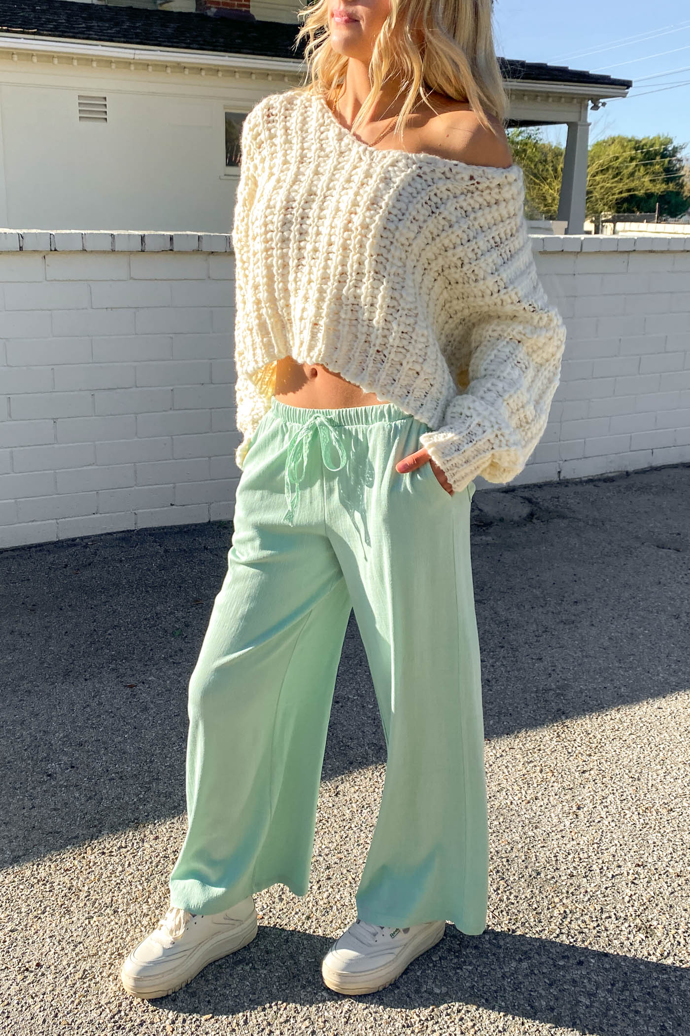 Person wearing a white chunky knit sweater and light green pants outdoors.