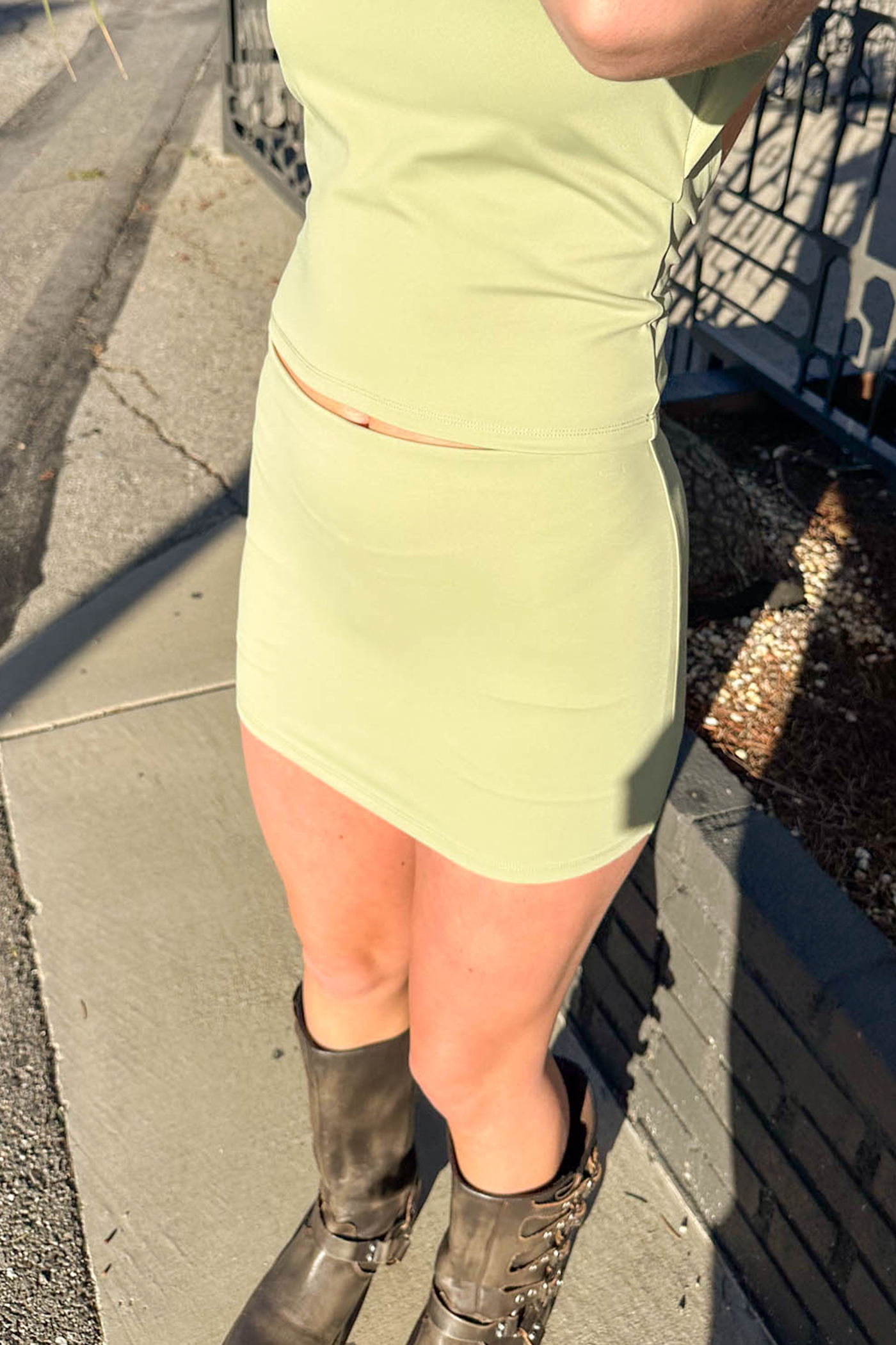 Person wearing a green dress and black boots on a sidewalk.