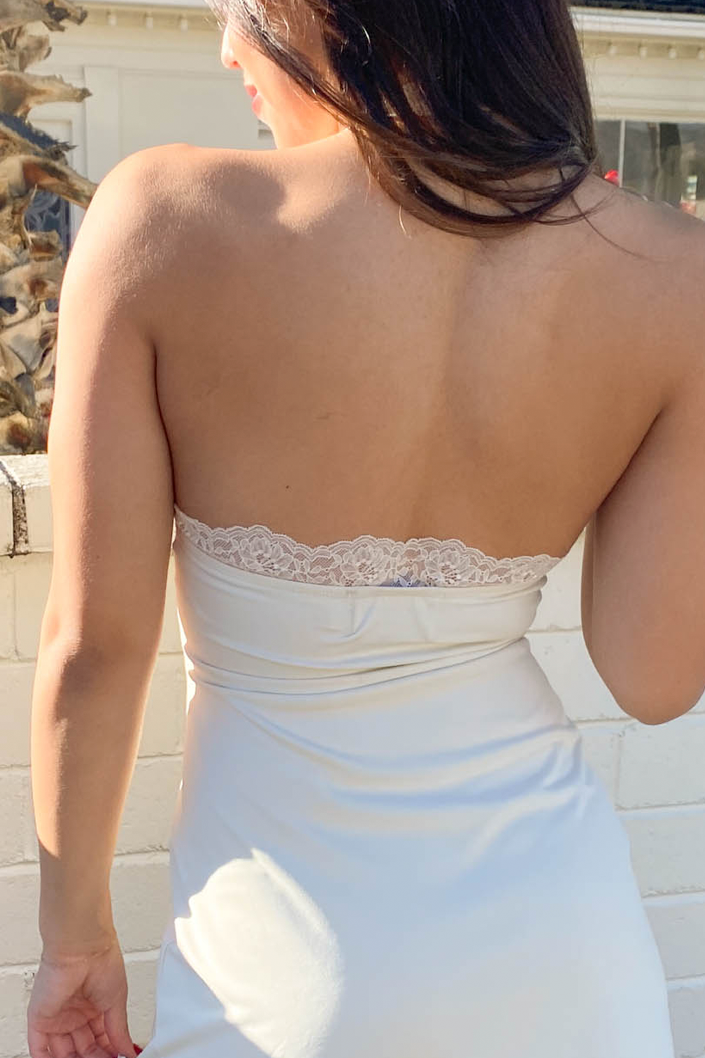 Woman wearing a strapless white dress with lace detailing in an outdoor setting.