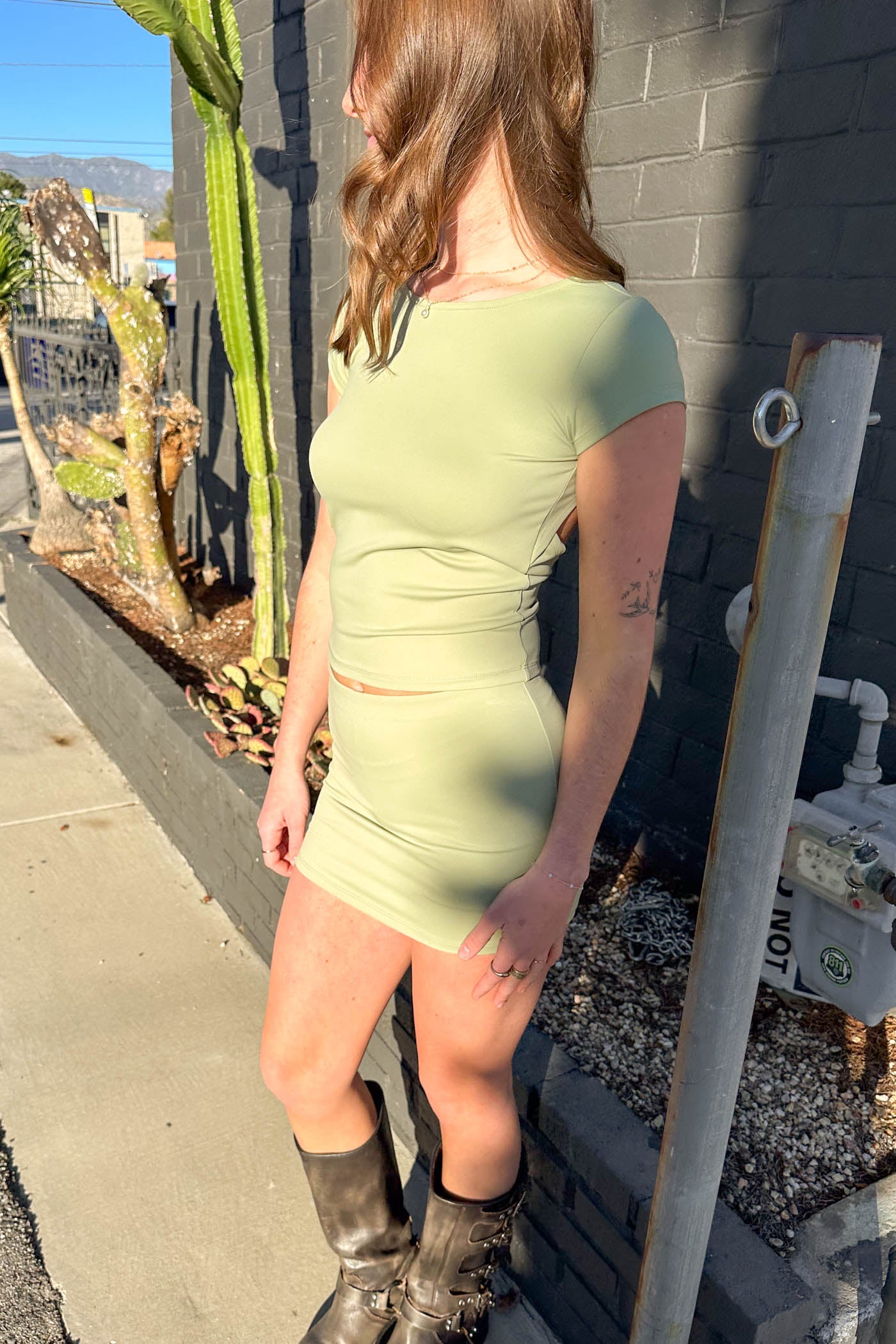 Woman in a green dress standing against a gray wall with cacti in the background