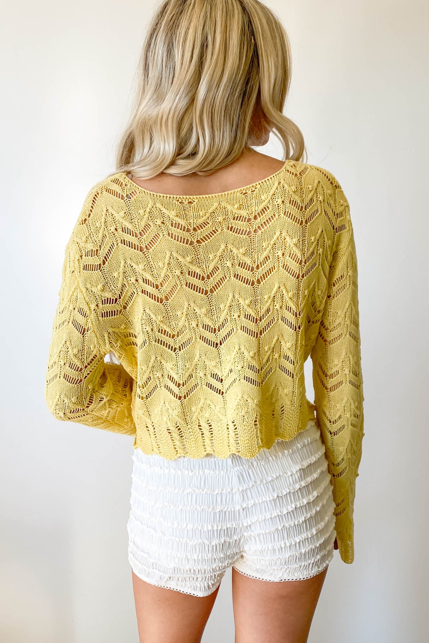 Person wearing a yellow lace top and white shorts against a plain background