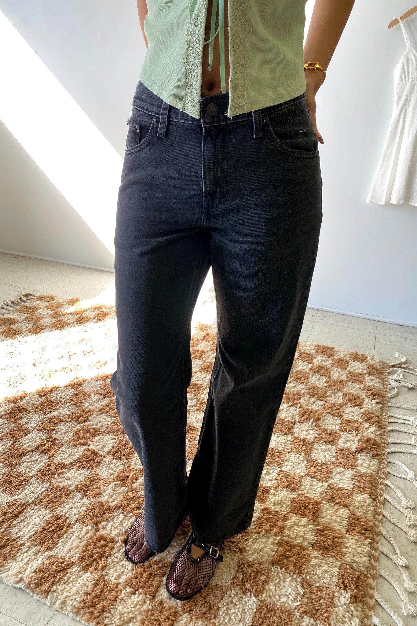 Person wearing dark jeans and a light green top on a checkered rug.