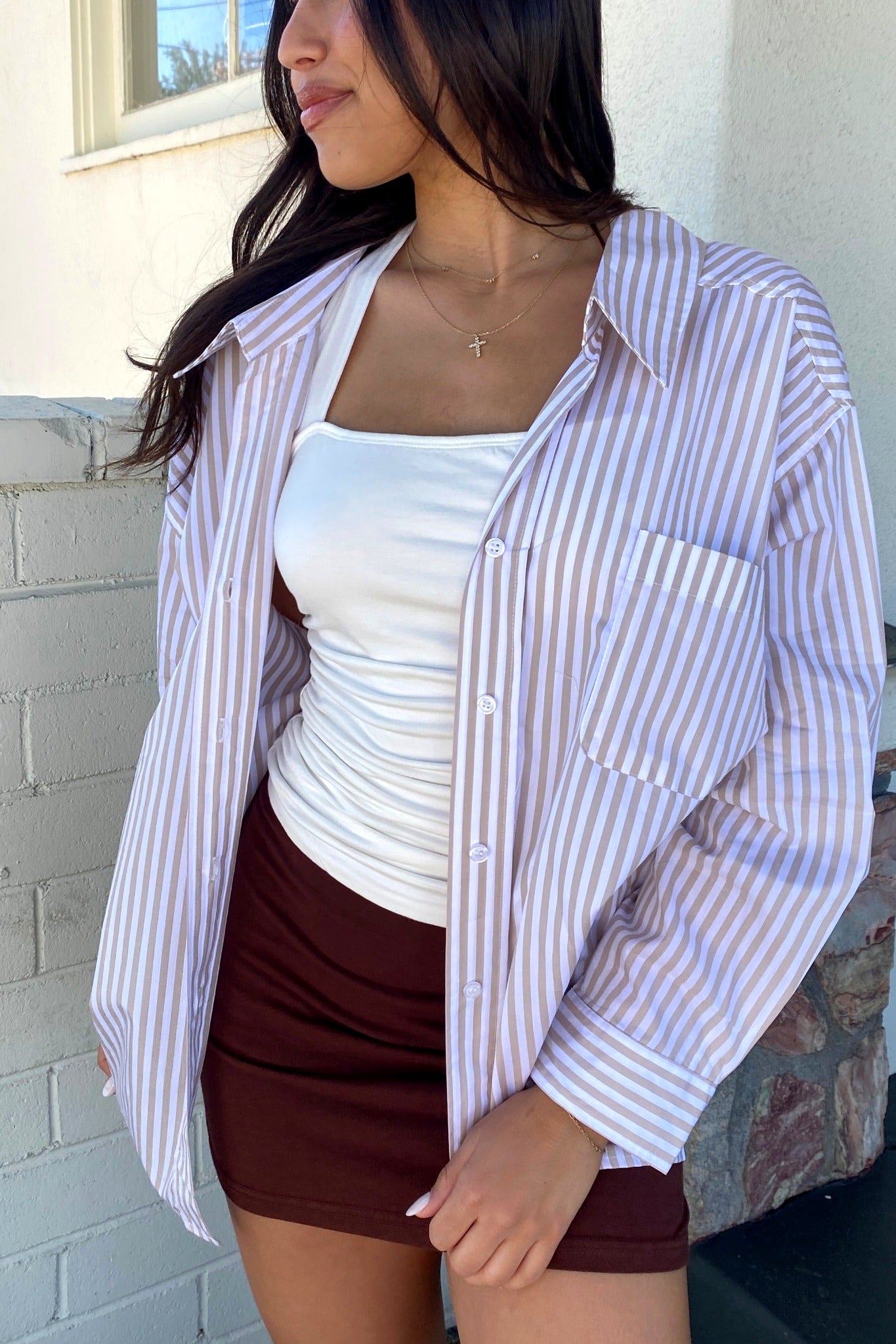 Woman wearing a striped shirt over a white top and maroon skirt against a brick wall.