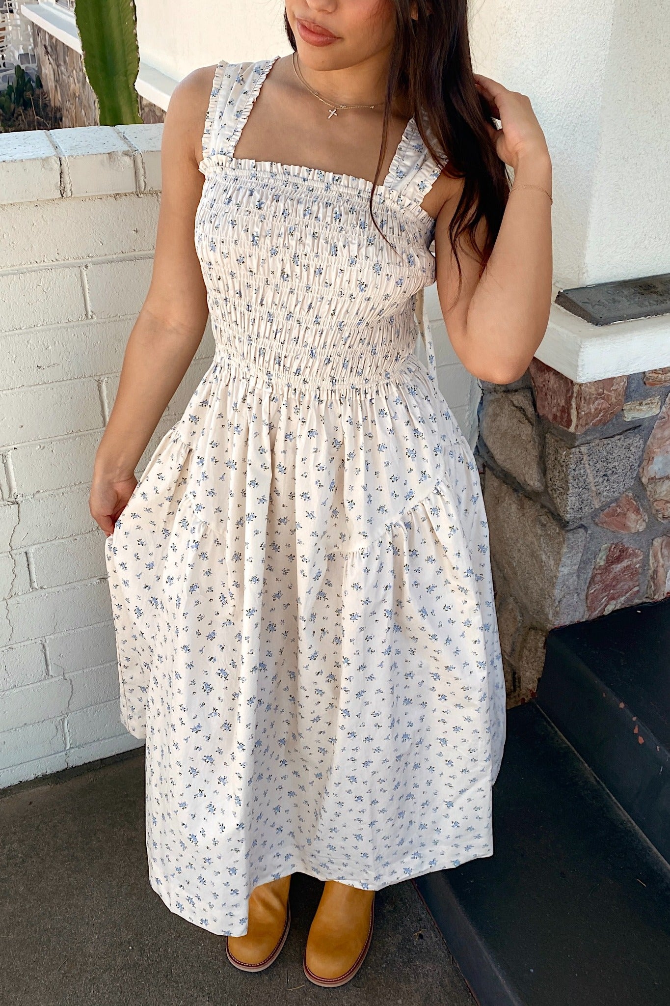 Woman wearing a white floral dress standing against a white wall.